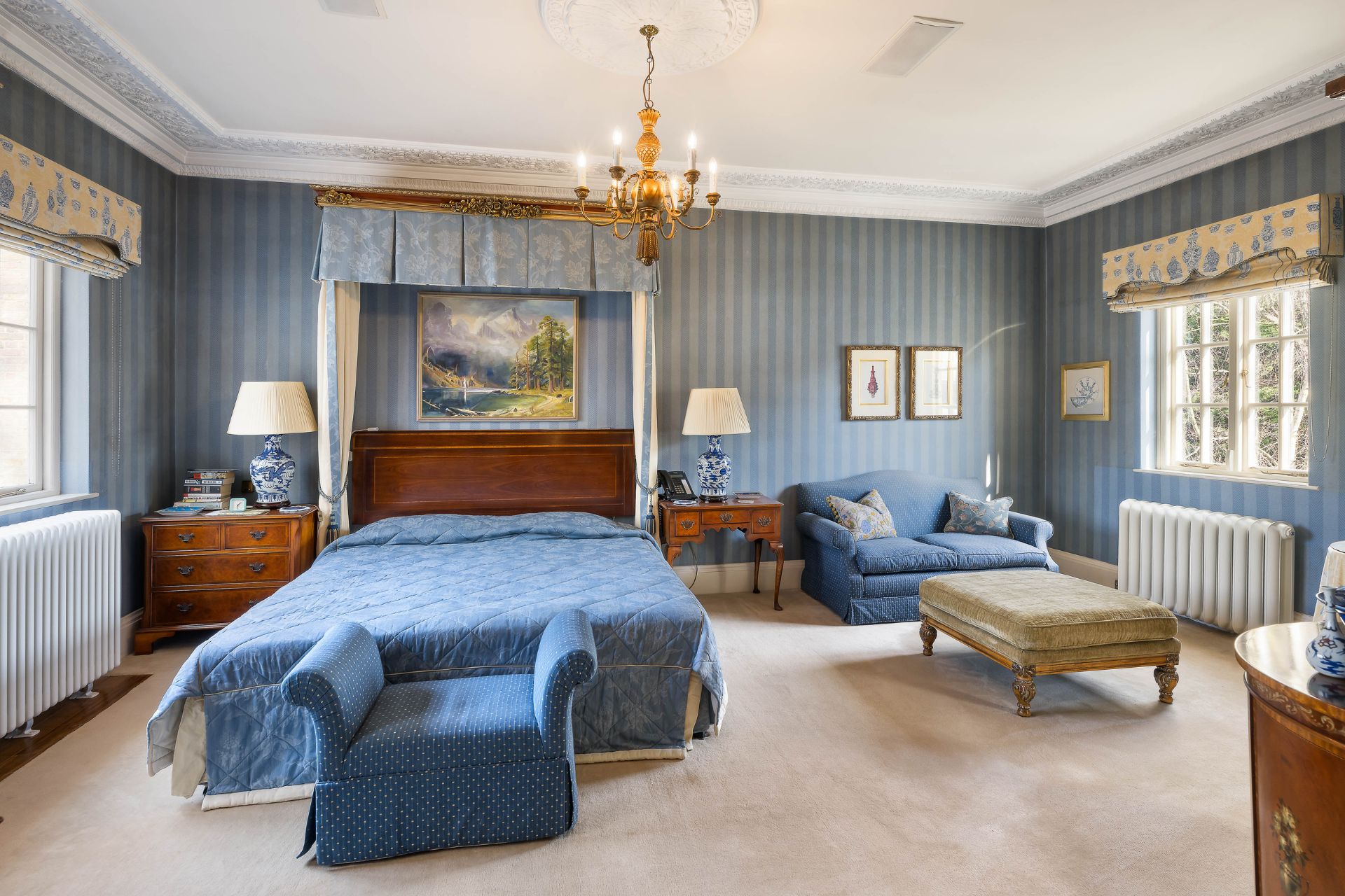 Bedroom with blue striped wallpaper, a blue bedspread and a gold chandelier.