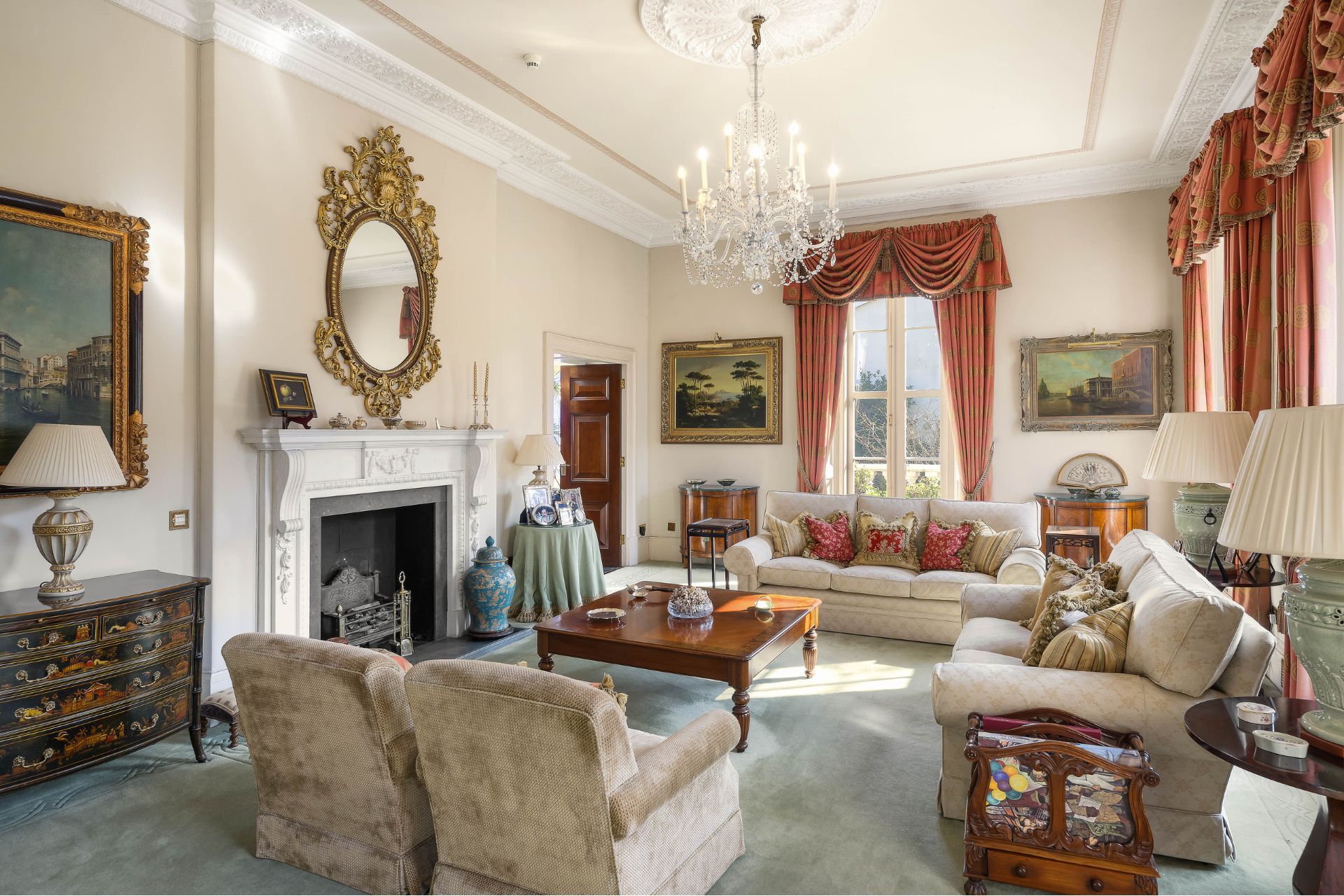 Living room with cream sofas, a marble fireplace, a gilt mirror and a chandelier