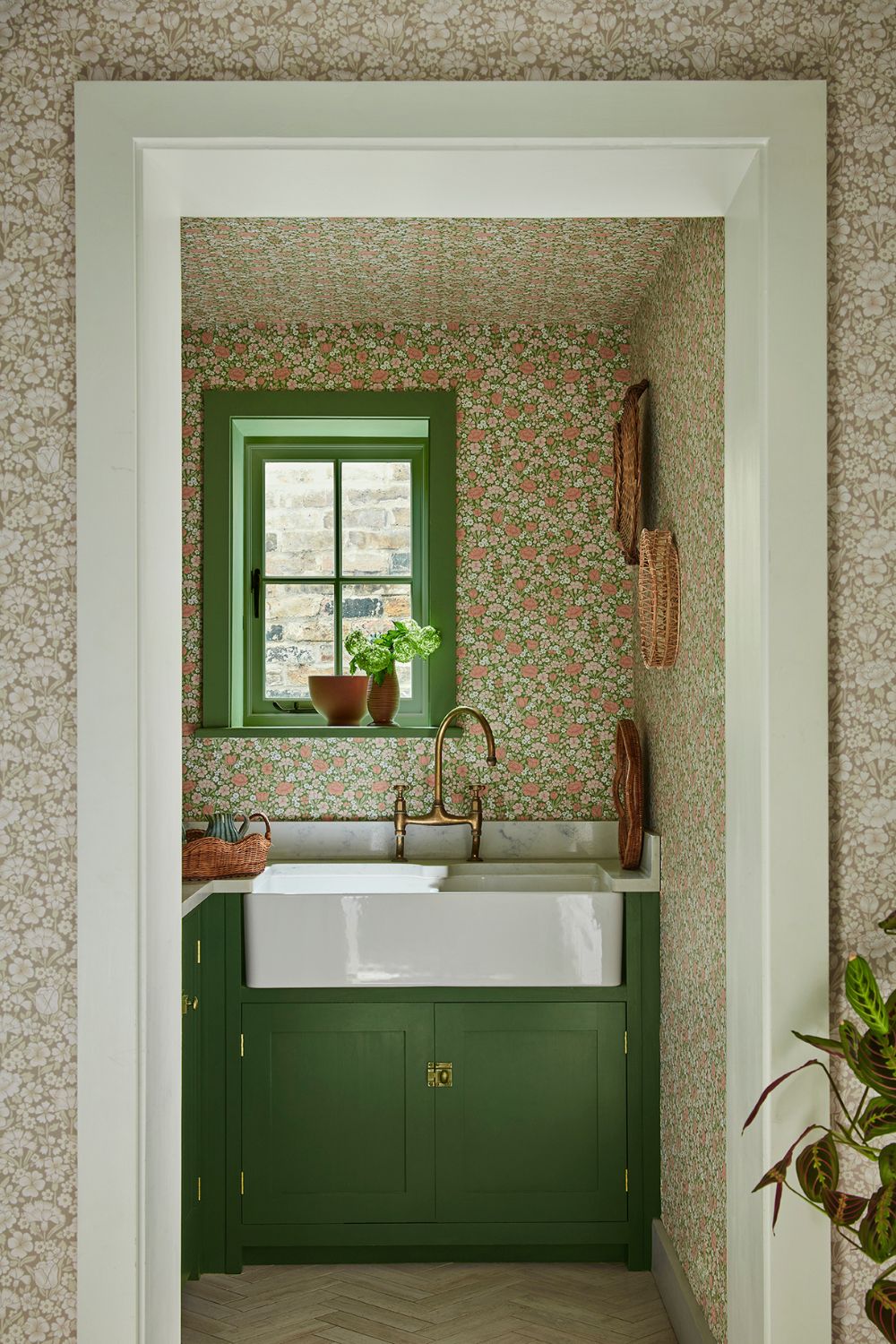 Utility room with pink floral wallpaper, sage green cabinets and white worktops