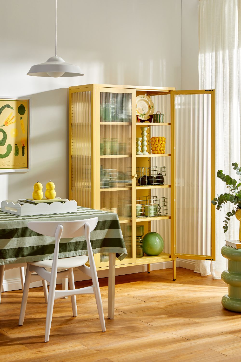 Dining room with pale yellow tall shelving unit, white dining furniture and a green and white striped tablecloth