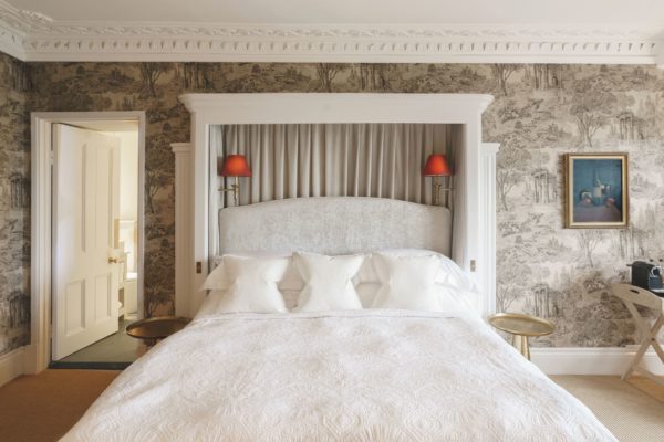 Hotel bedroom with large white bed and taupe floral wallpaper