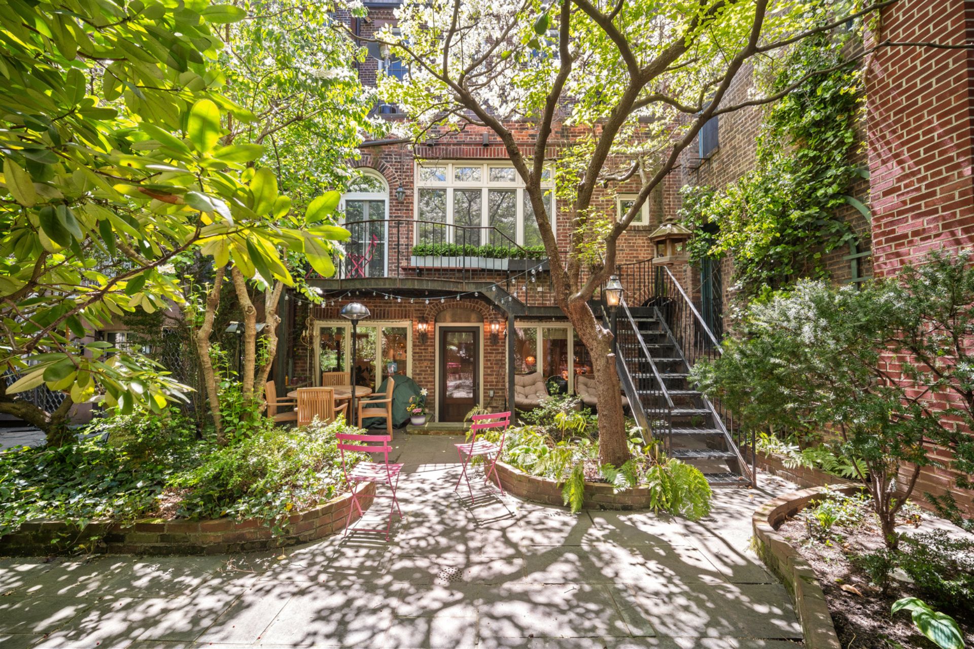 Leafy rear garden with flower beds, trees and a stone patio area