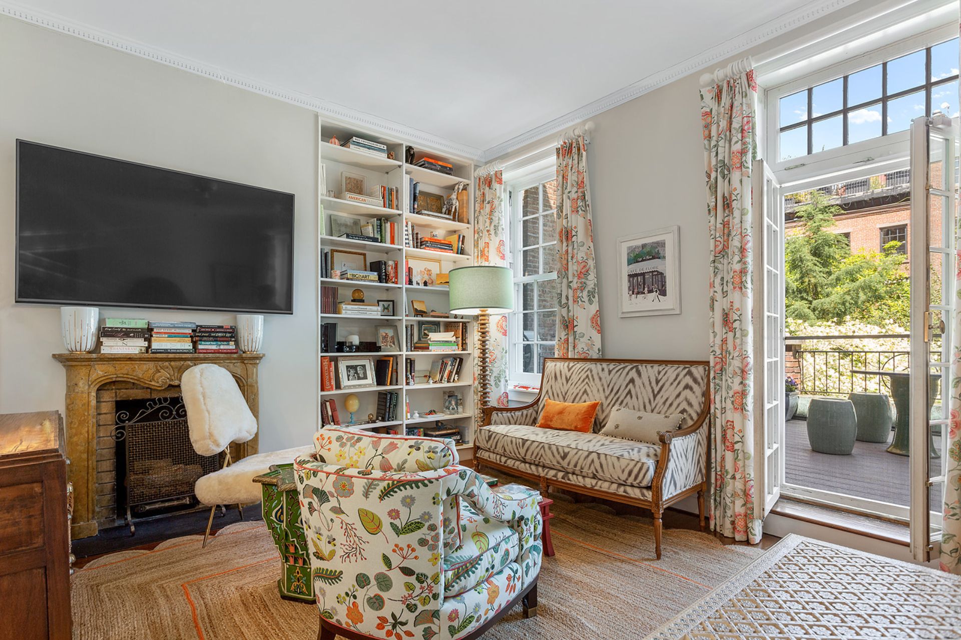Living area with floral armchairs, a built-in bookcase, floral curtains and doors leading onto a terrace