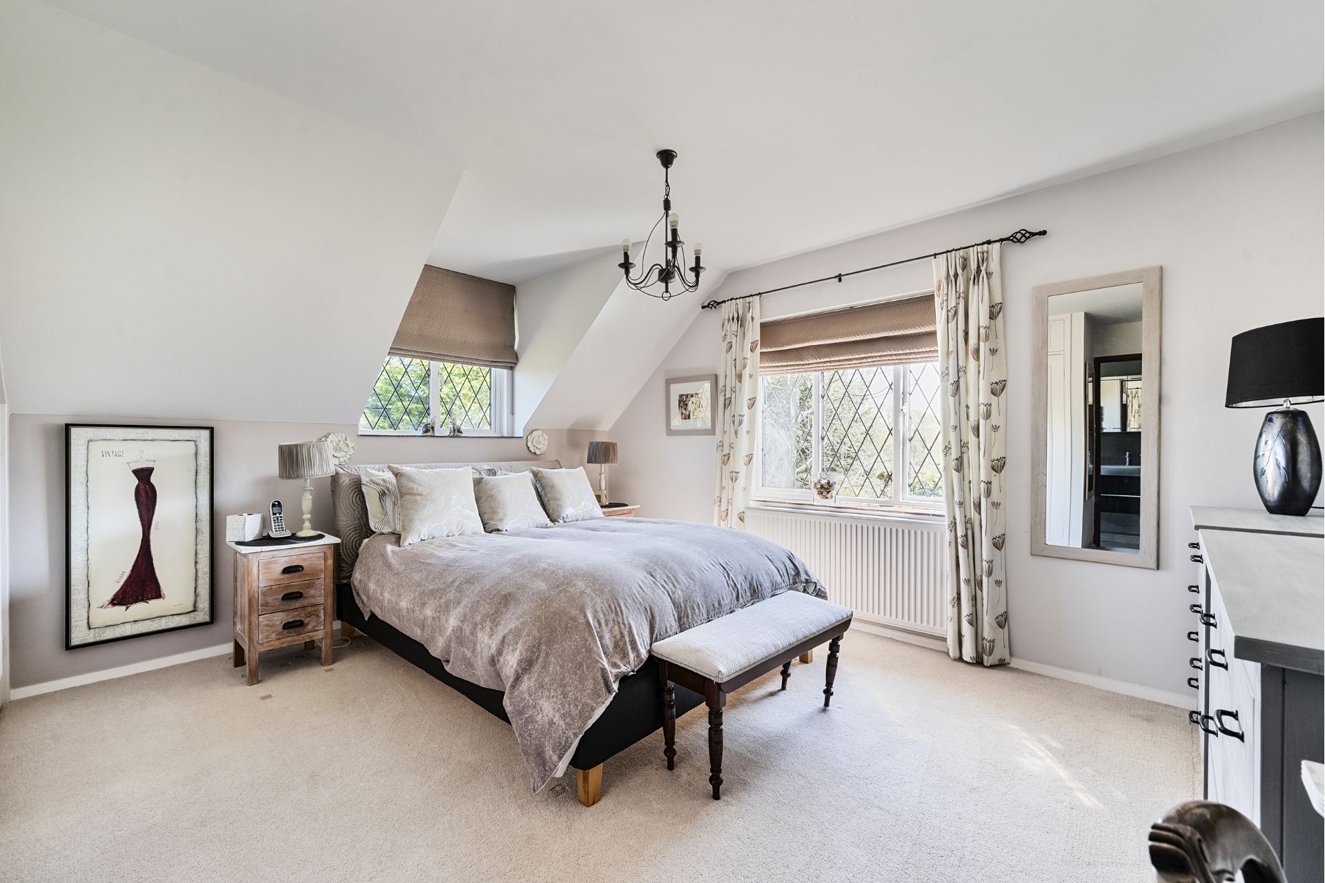 Bedroom with leaded windows, cream carpets, grey bedding and a chandelier