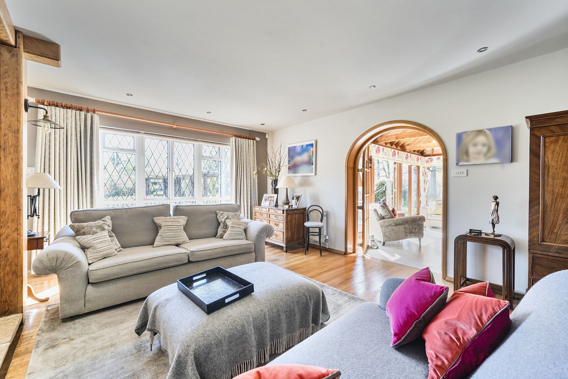 Living room with gret sofas, pink and orange cushions, and a wooden archway leading into a dining area