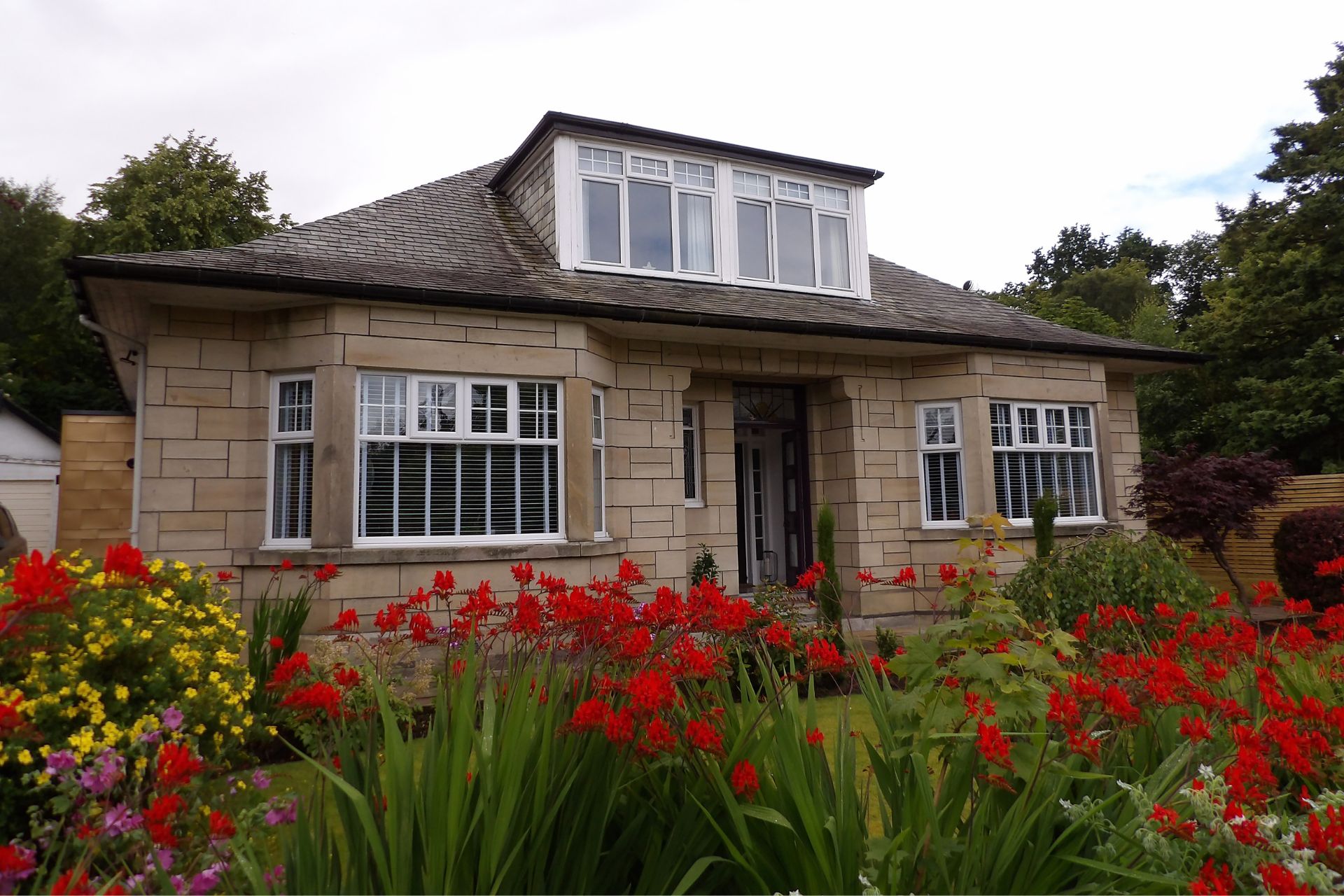 Sandstone bungalow with red flowers growing outside