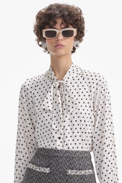 Curly haired model wearing a black and white polka dot blouse