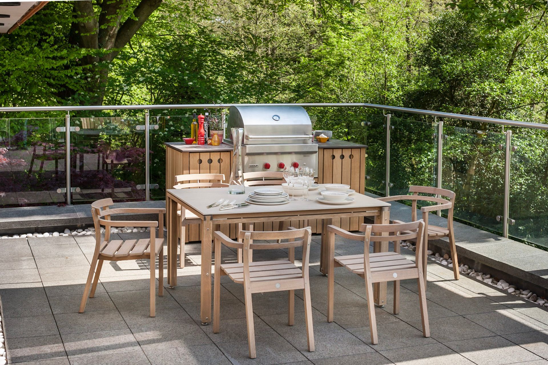 Outdoor kitchen with wooden cabinets, stainleess steel grill, and wooden dining furniture