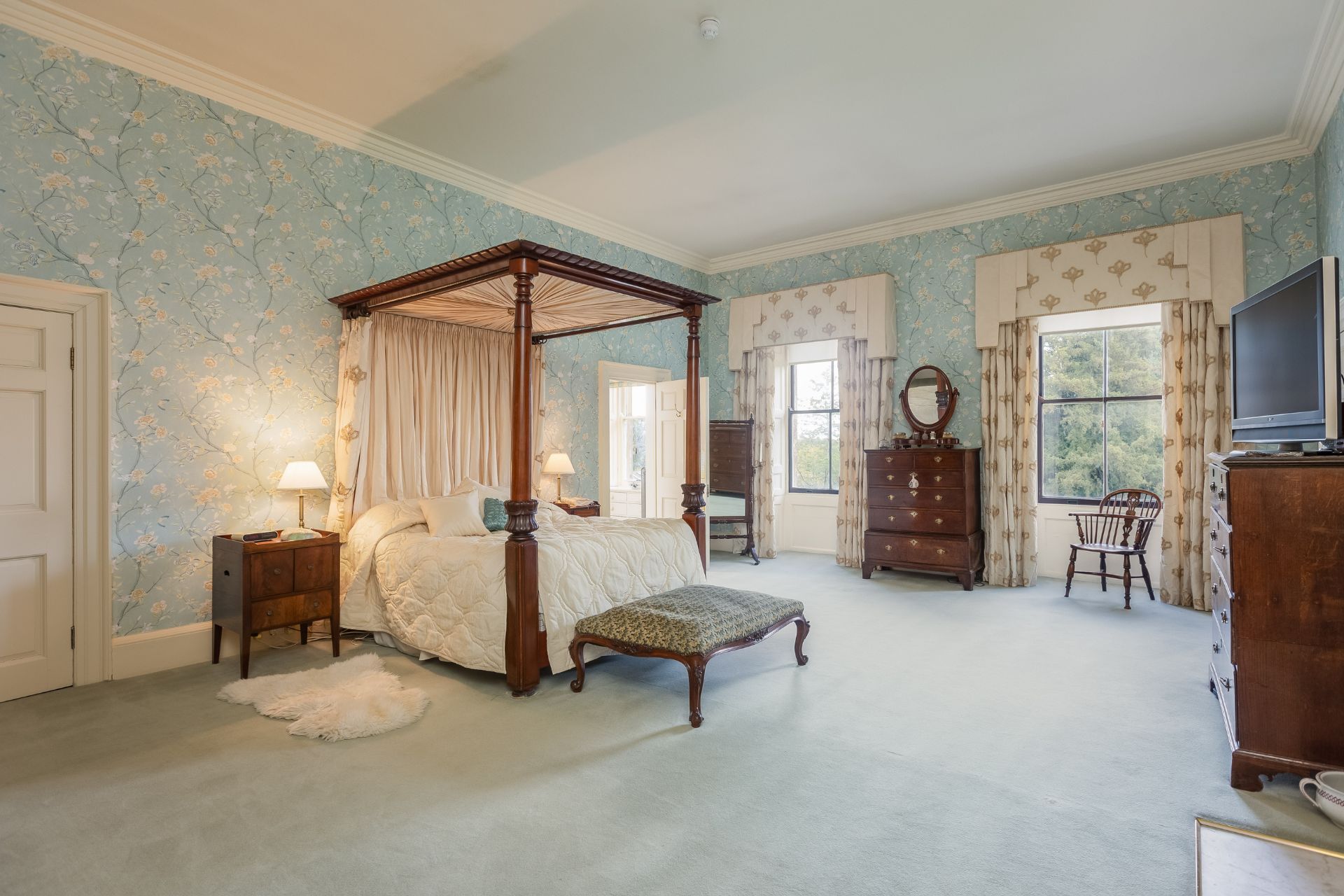 Bedroom with four poster bed, pale blue floral wallpaper, and cream carpet