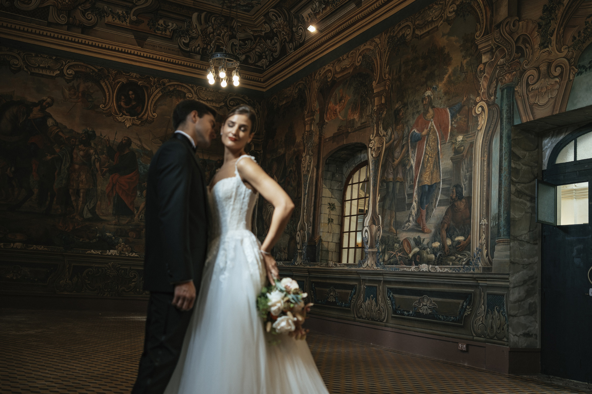 A bride and groom standing in an opulently painted room
