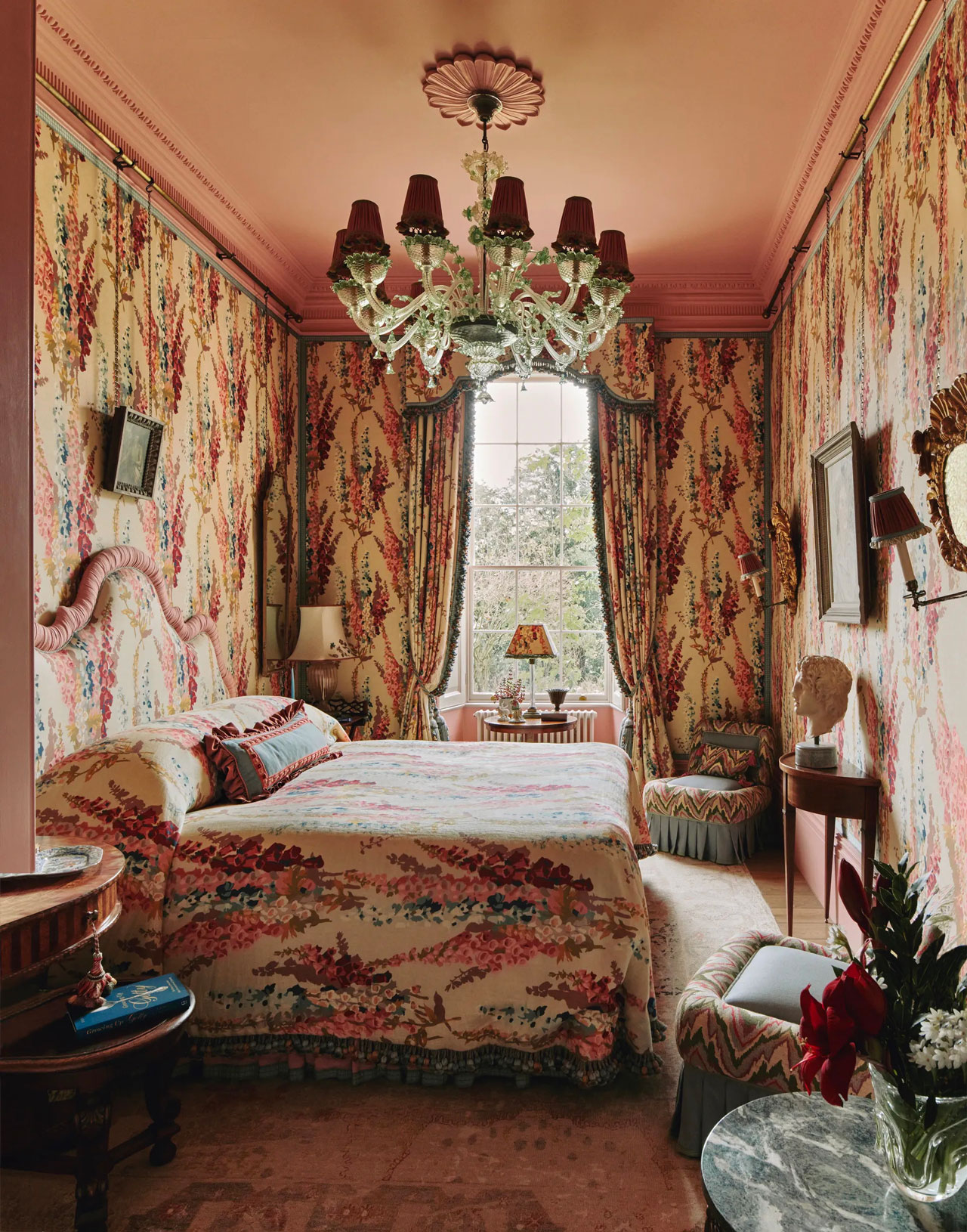 Floral bedroom with headboard that matches the wallpaper. A window at the end with matching curtains.
