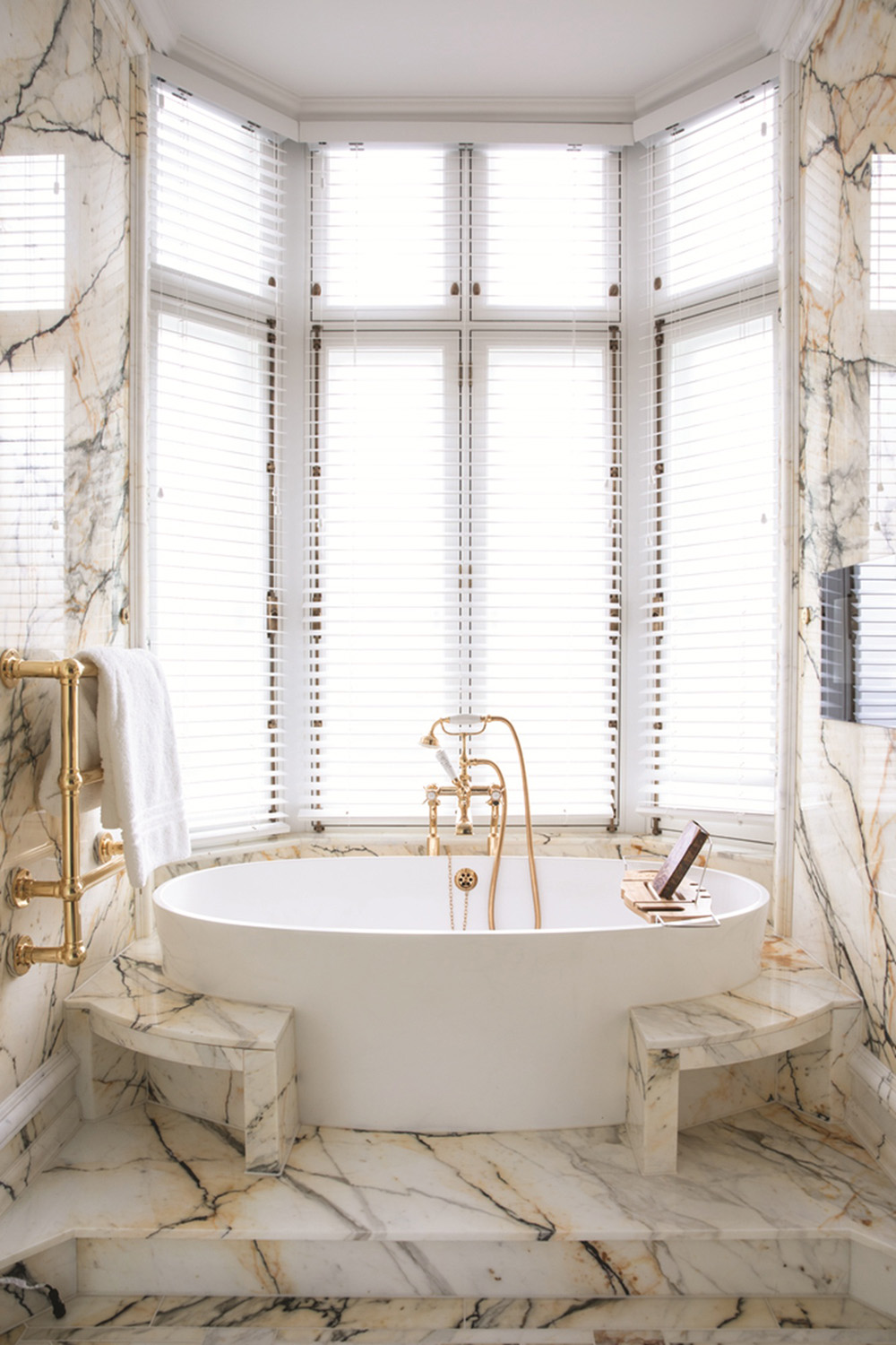 A bathtub surrounded by marble in a bay window