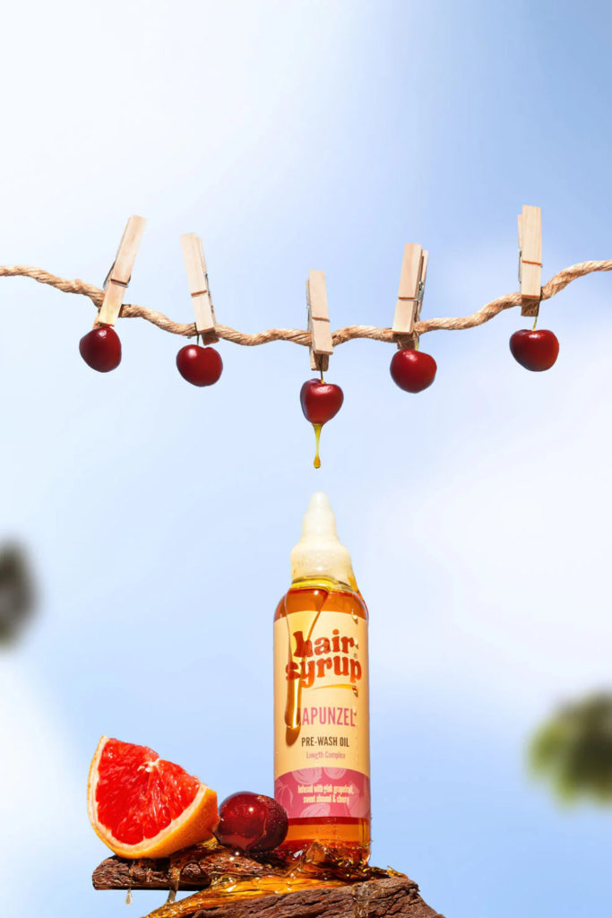 Hair syrup set amongst fruit with strong of cherries held above