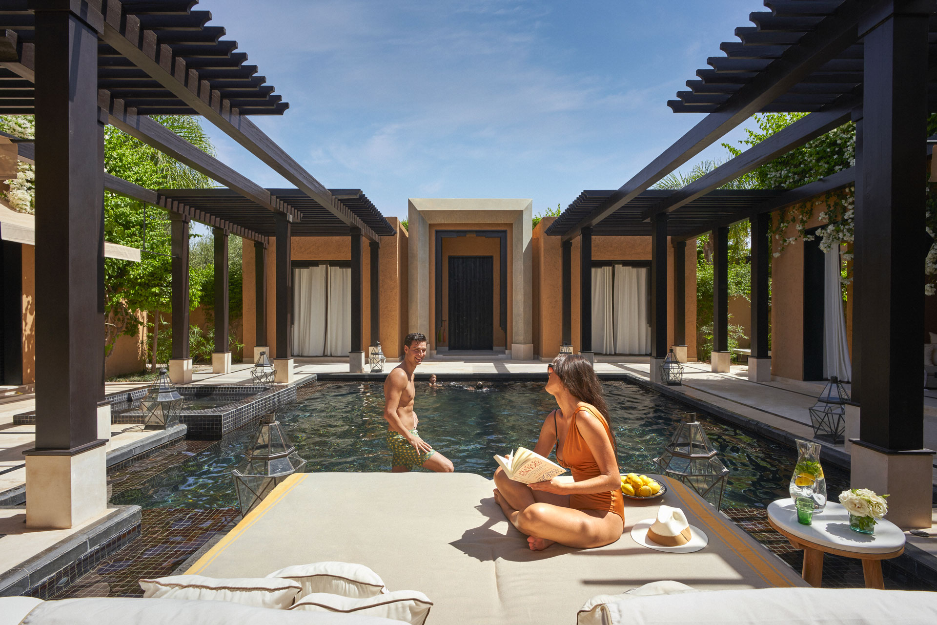 The villa at the Mandarin Oriental by daytime with a person jumping into the pool, as a woman reads by the side.