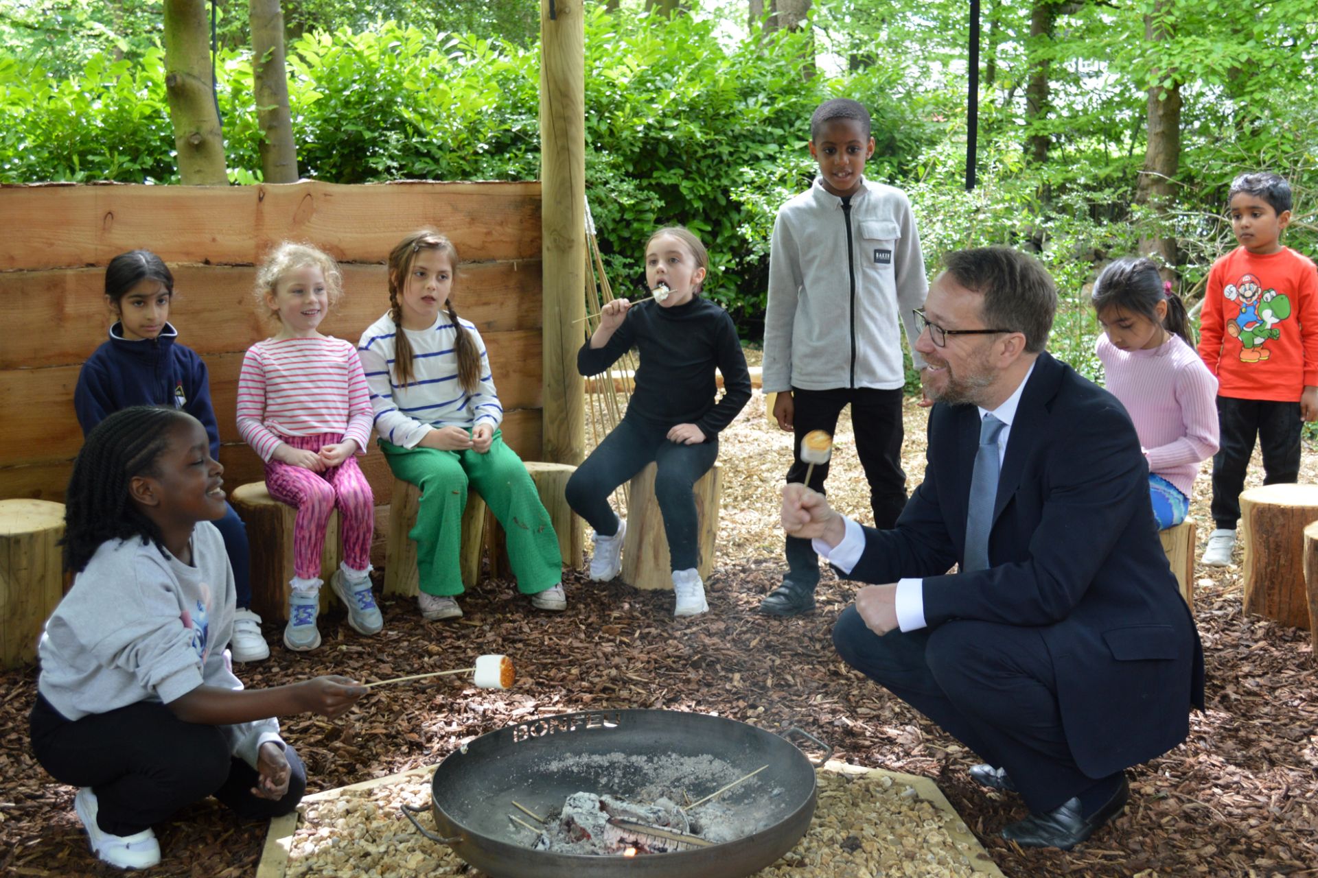 Bolton School governor toasting marshmallows outside with young pupils