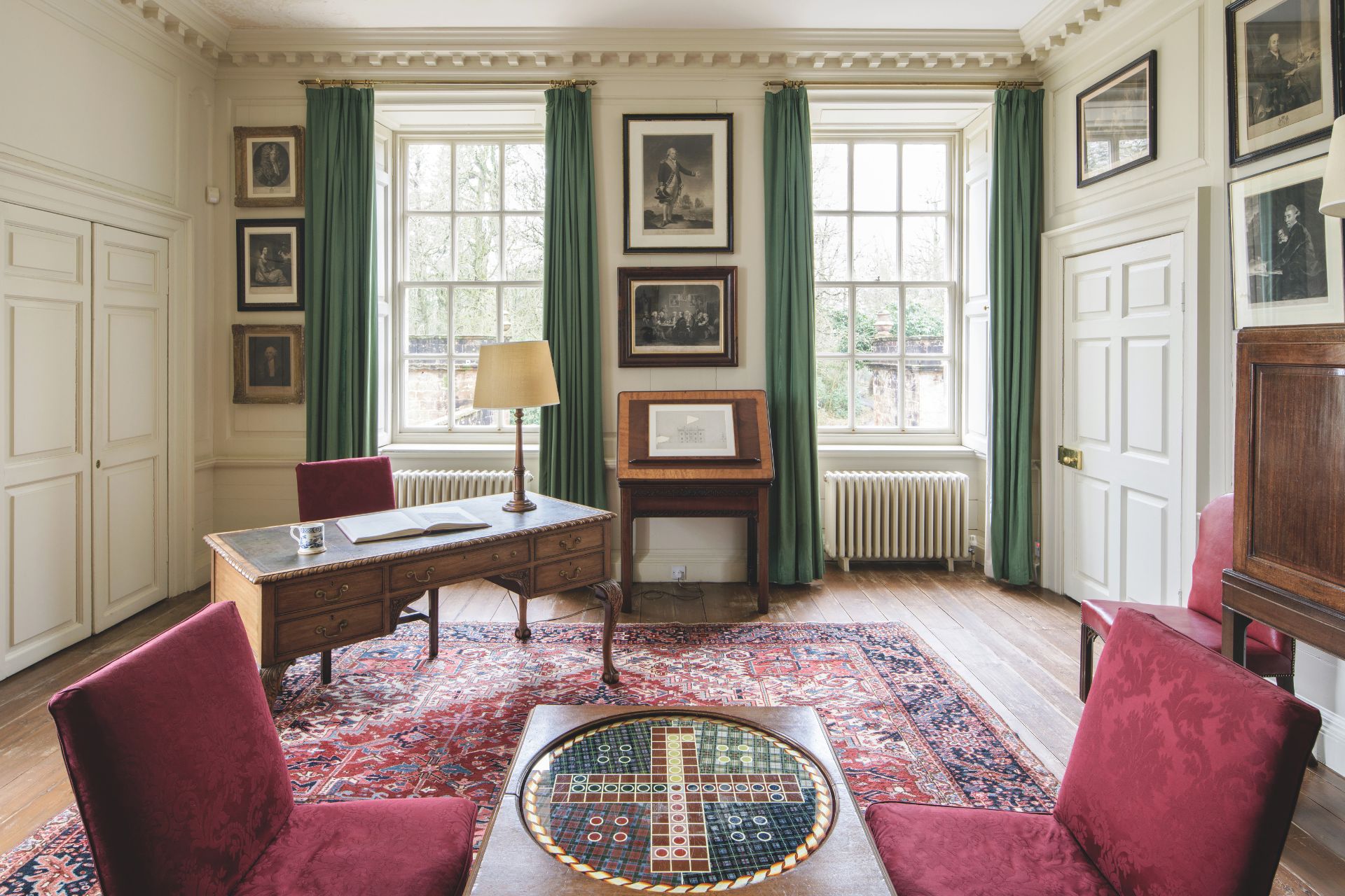 Drawing room with red Persian rugs, red velvet chairs and a wooden desk