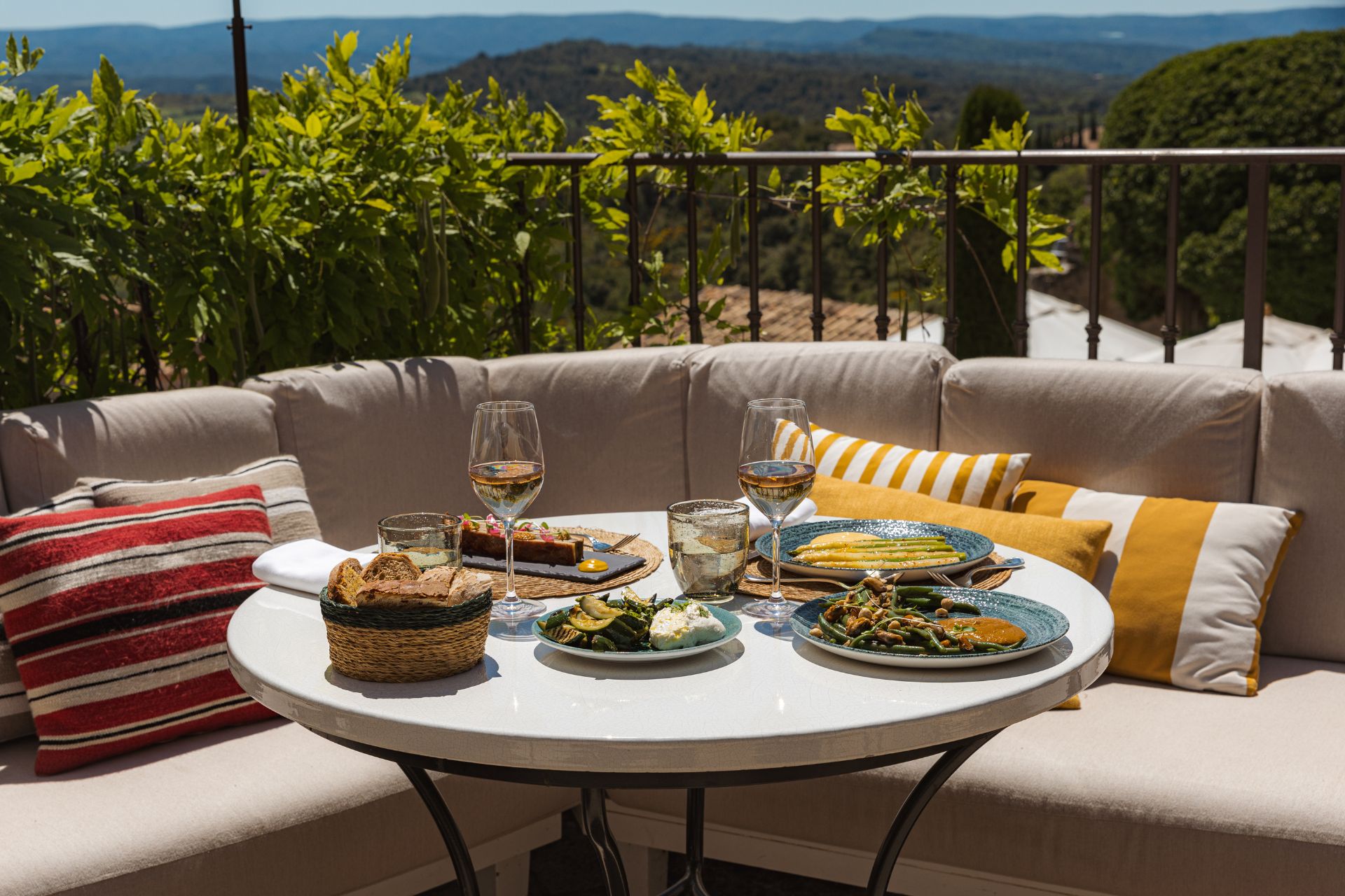 Outdoor dining area with cream sofa, red and yellow striped cushions, and views of Provence
