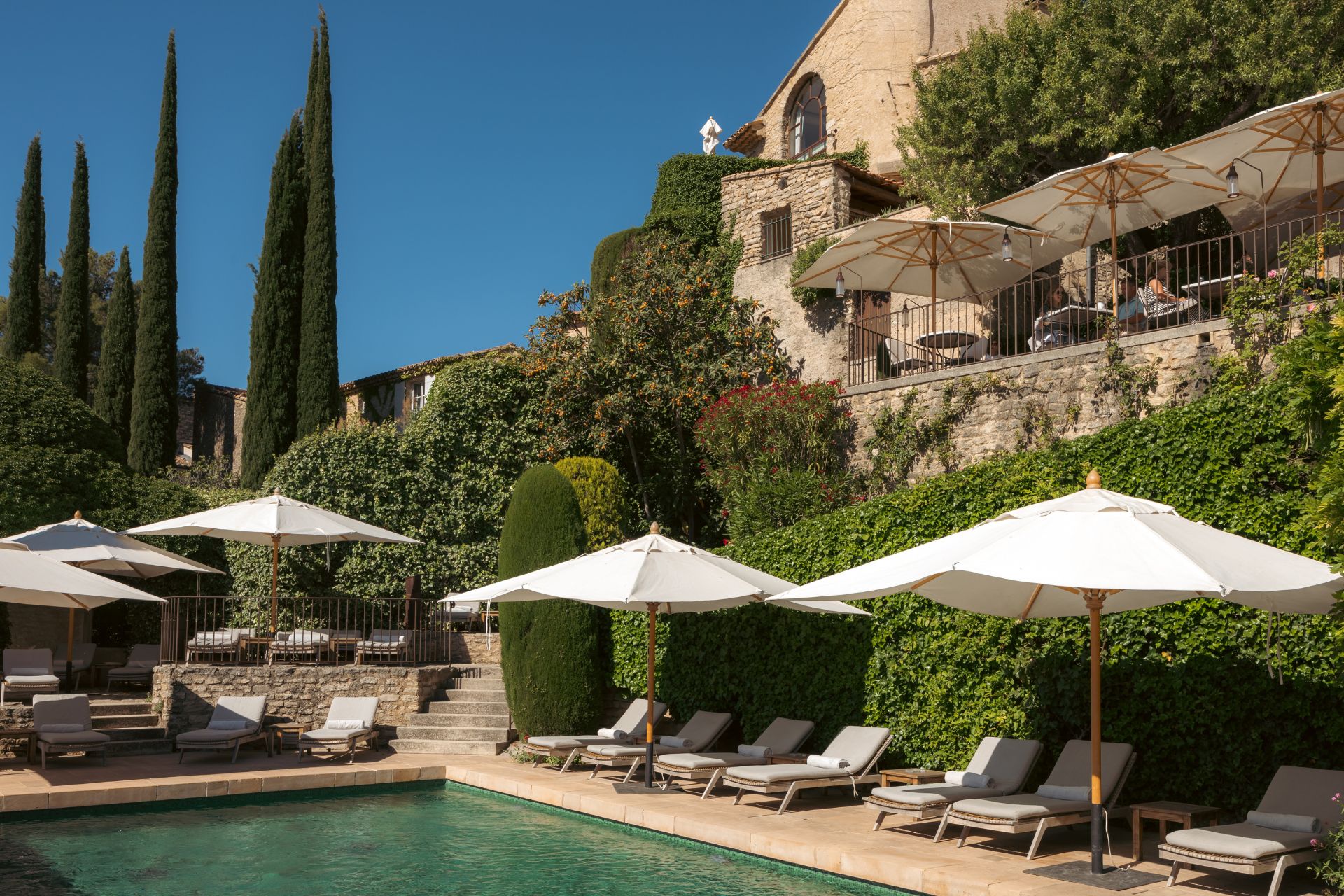 Hotel pool on stone terrace with white outdoor furniture and ivy-clad walls