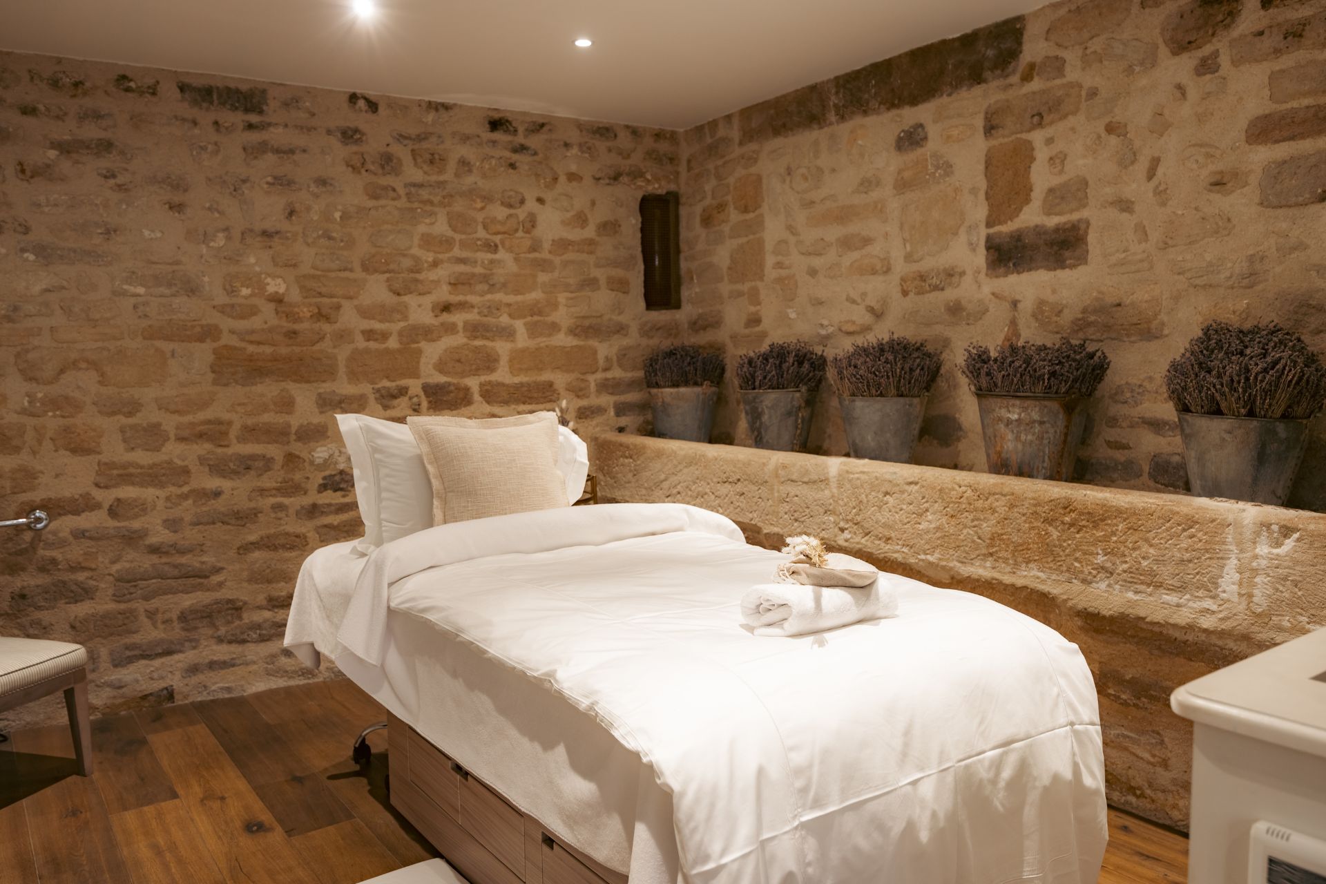 Spa treatment room with brick walls and cream linen, with silver pots of lavender lining one wall