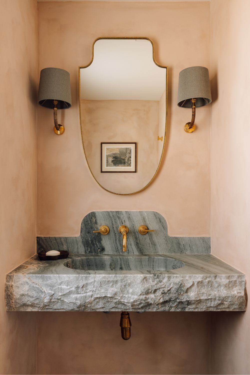 Pale pink powder room with gret marble vanity and grey sconces