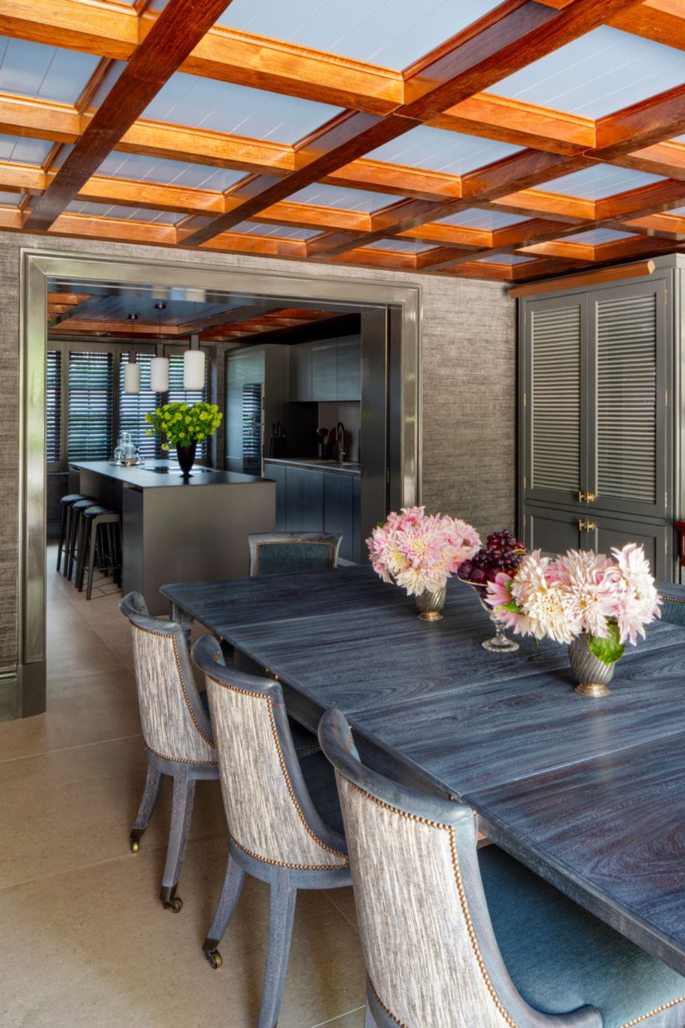 Dining om with wooden grid ceiling beams, a dakr grey marble table and ceam chairs