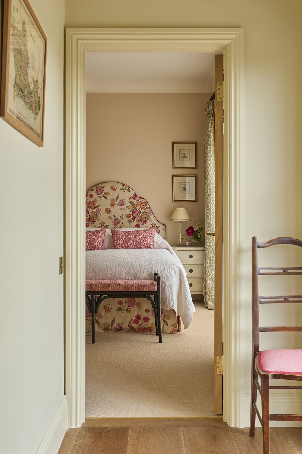 Cream hallway with a wooden chair and a doorway leading into a bedroom with a pink and cream floral patterned headboard