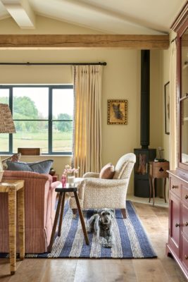 Barn conversion living area with a cream patterned armchair, blue and white striped rug, pale pink sofa and a woodburning stove