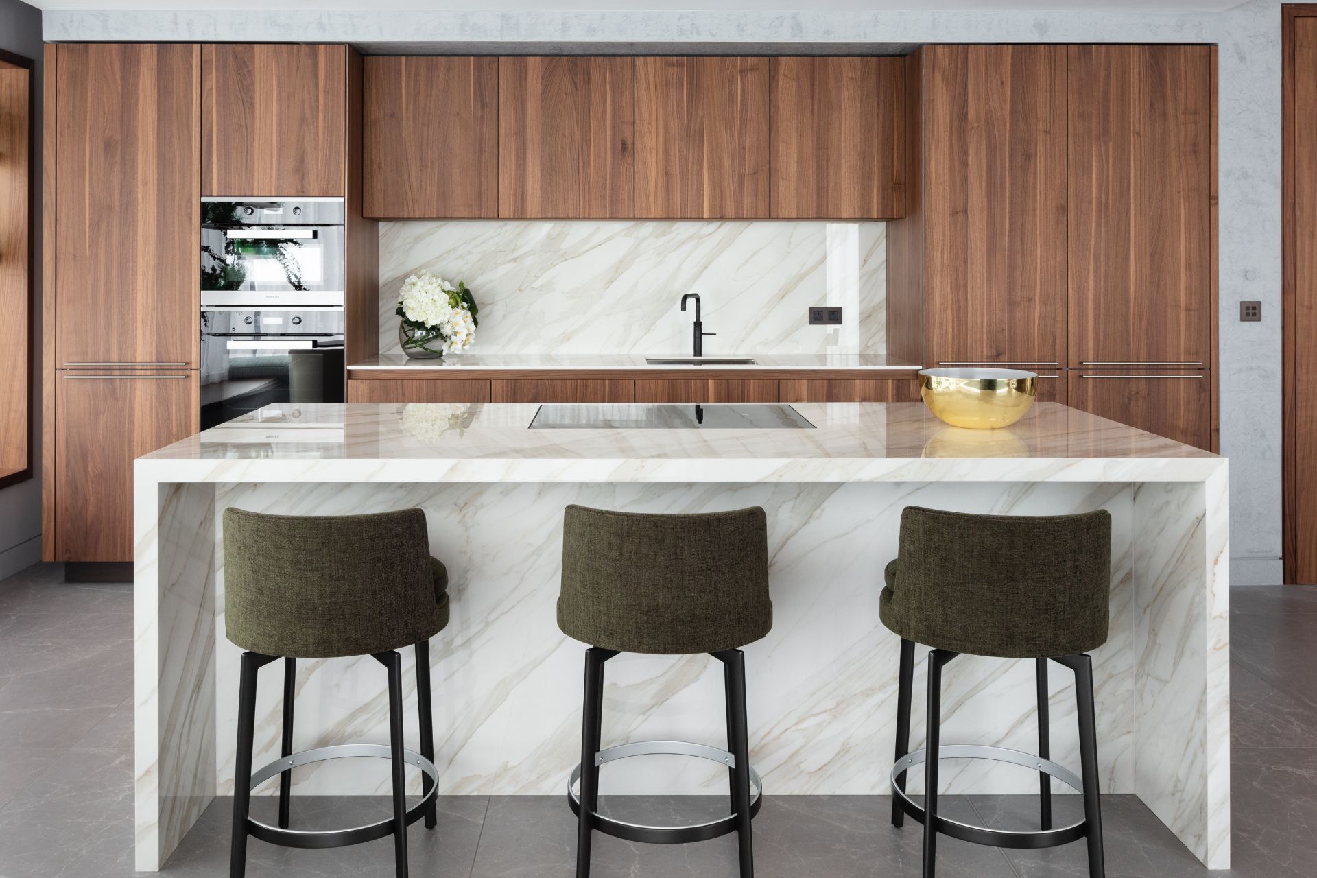 Dark wooden kitchen with white marble island and forest green velvet bar stools
