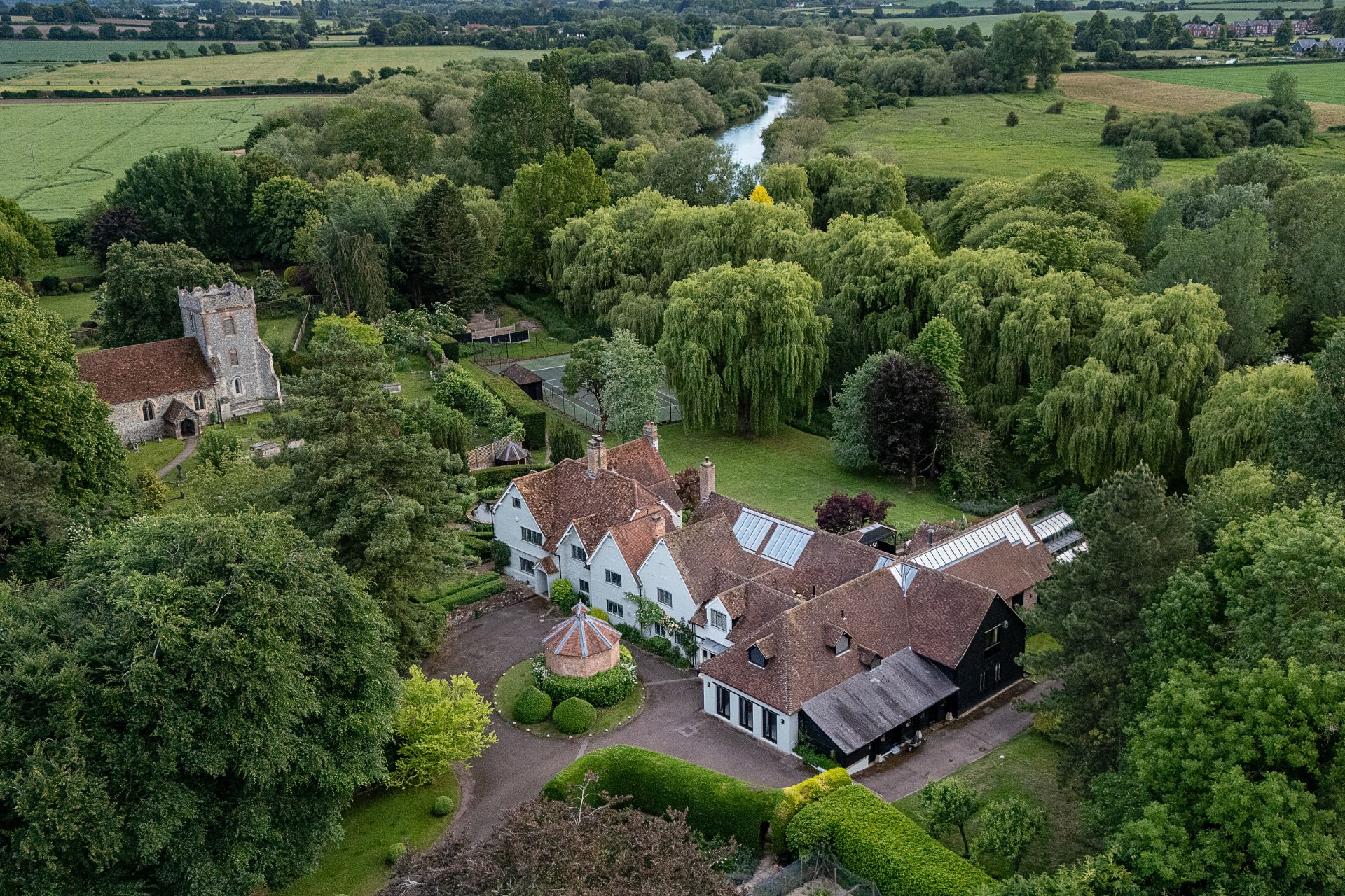 Aerial view of Grade II listed farmhouse with lawns and woodland surrounding it