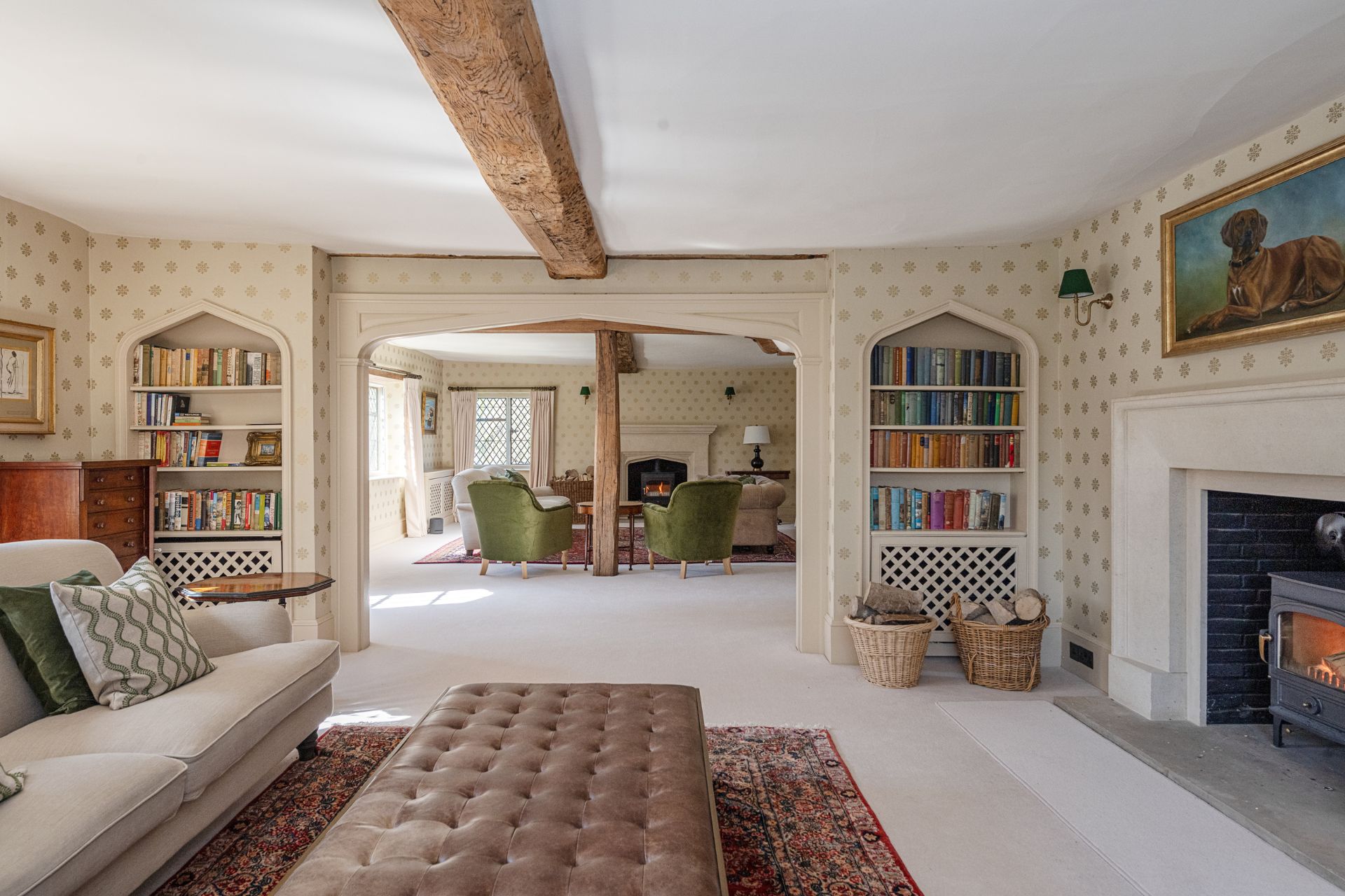 Living room with wooden beams, cream carpets, white sofas and green velvet chairs