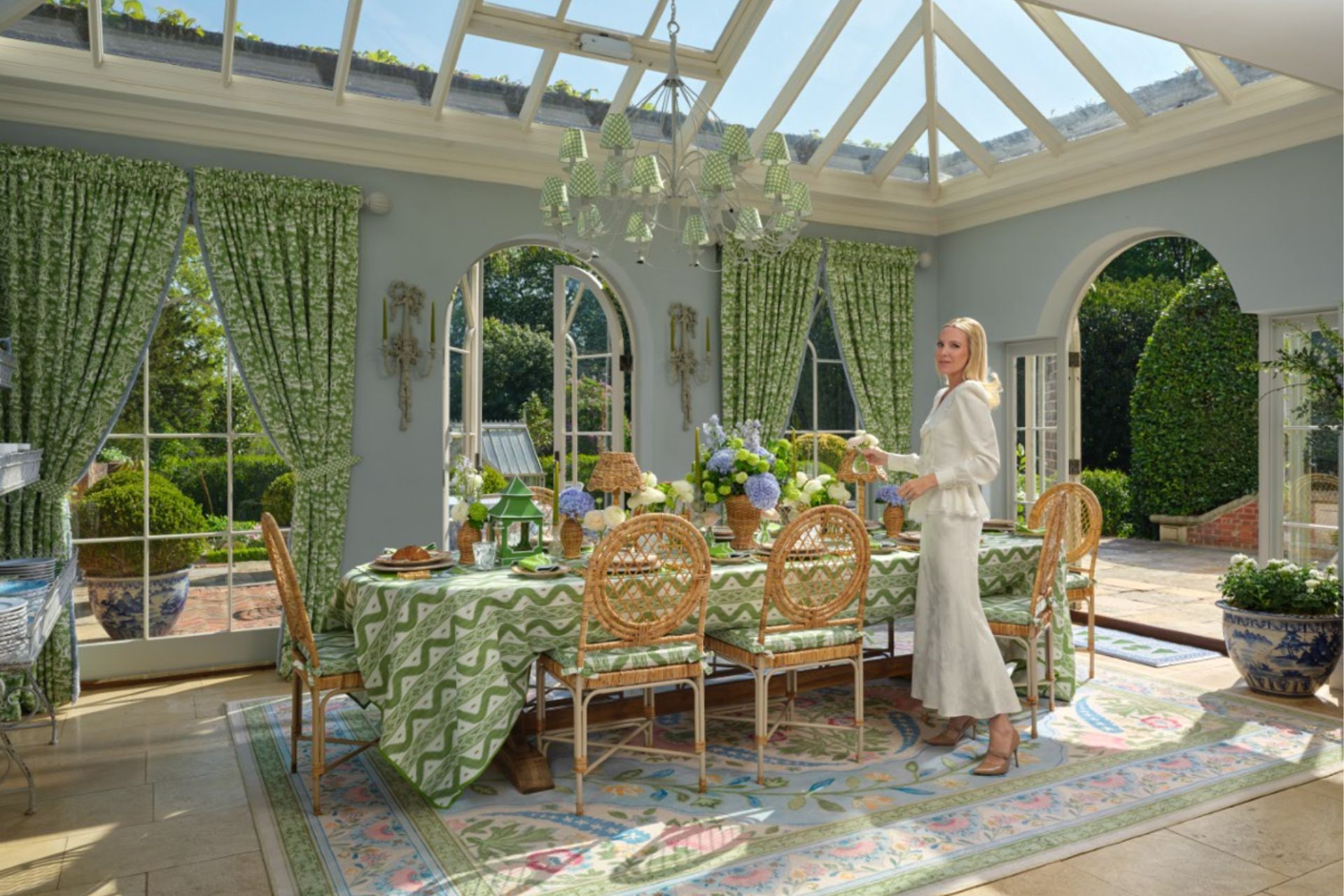 Orangery weith green tablescapr, pale white and green floral rug, and wooden chairs