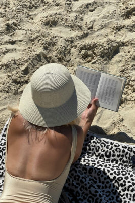 A woman reading on a beach in a sun hat