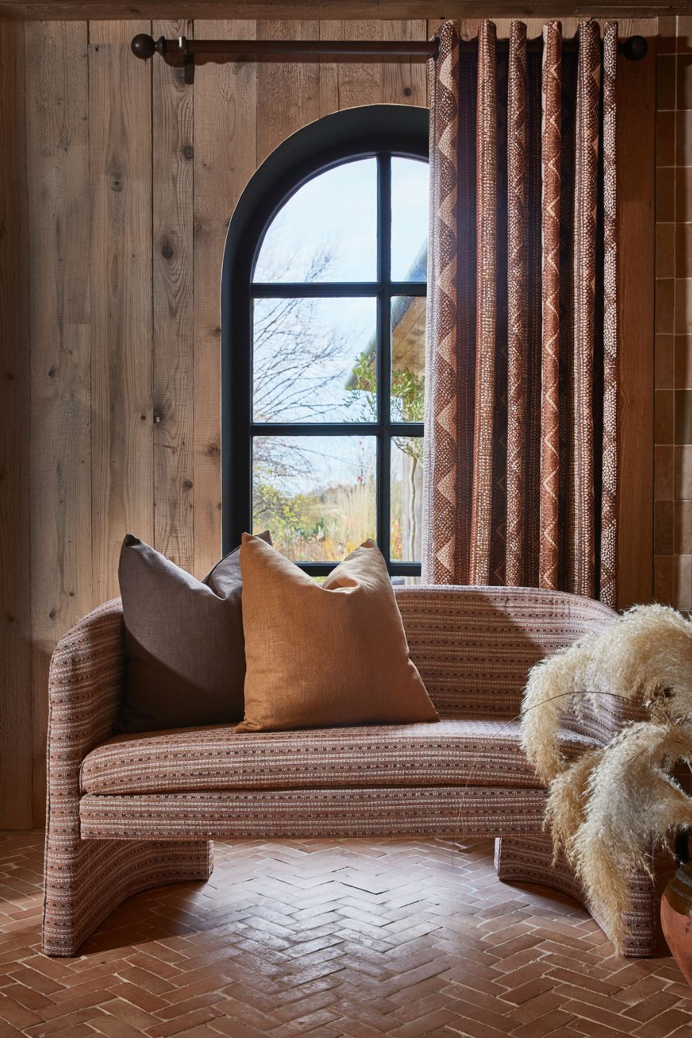 Wooden-clad room with arched Crittall window and patterned loveseat with orange and grey cushions