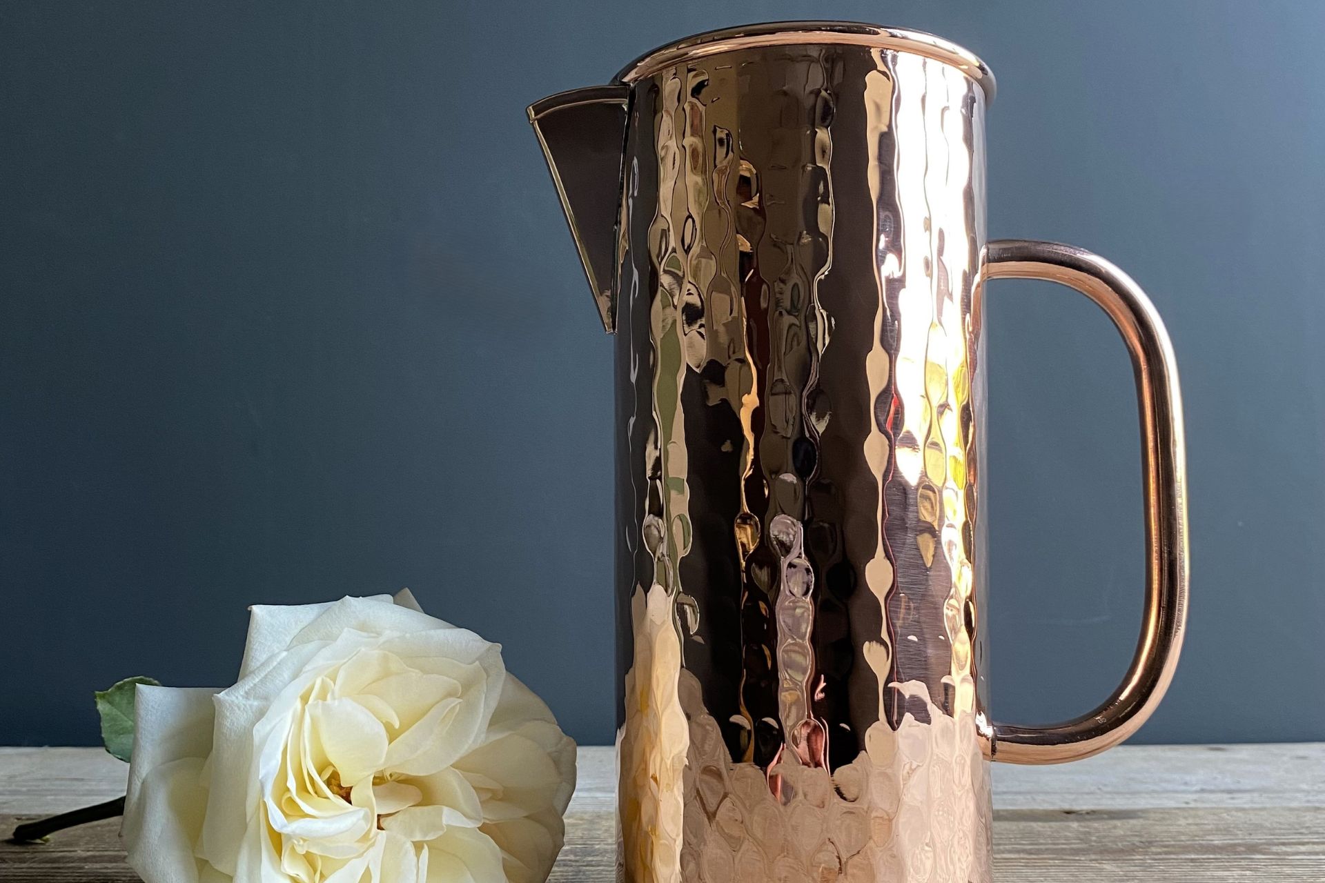 Tall copper jug next to single white rose