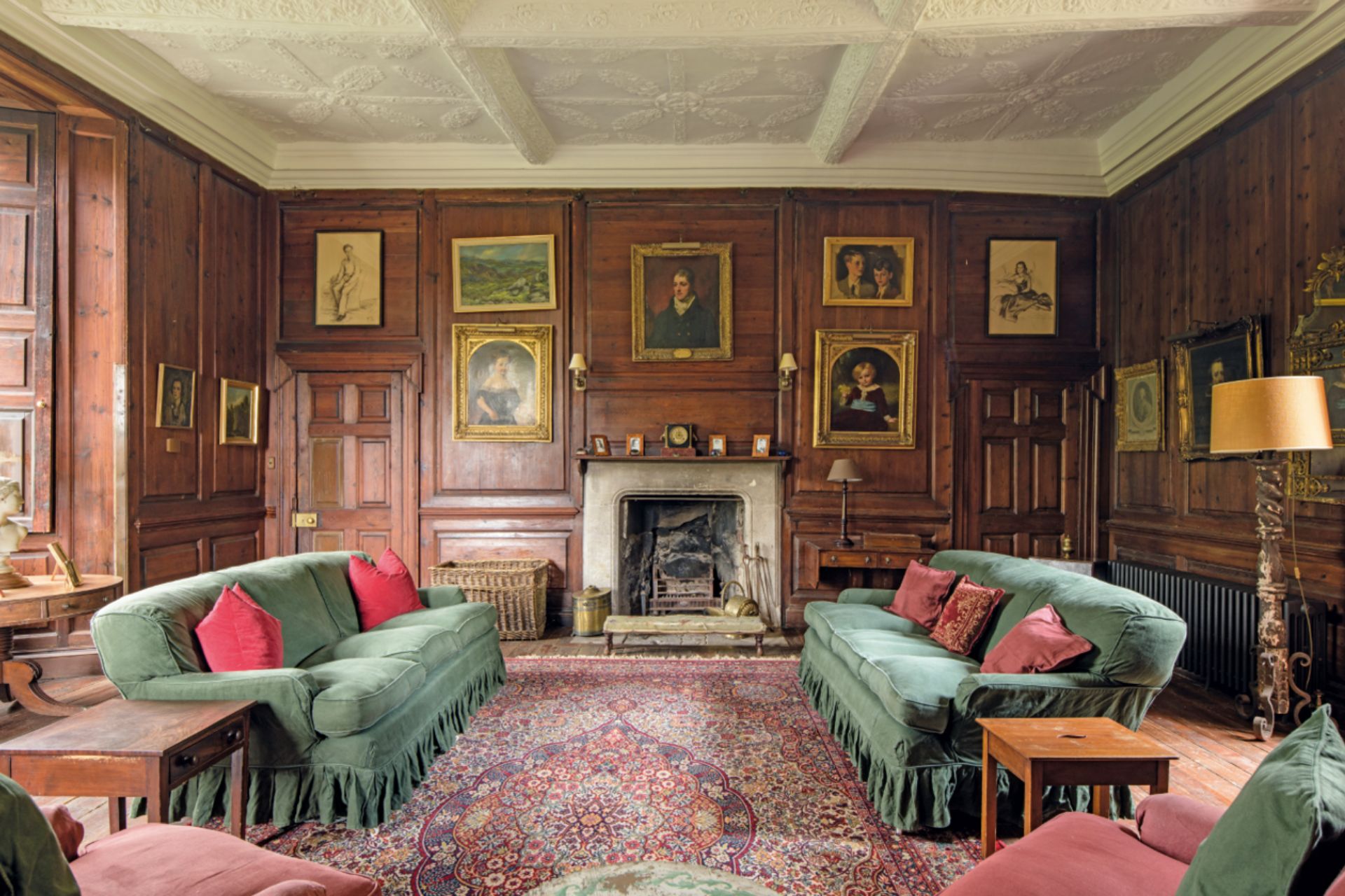 Wood panelled living room with green velvet sofas and a marble fireplace
