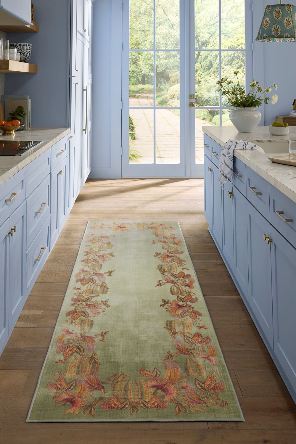 Galley kitchen with pale blue cabinets, white quartz worktops and a pale green rug with a gold floral border