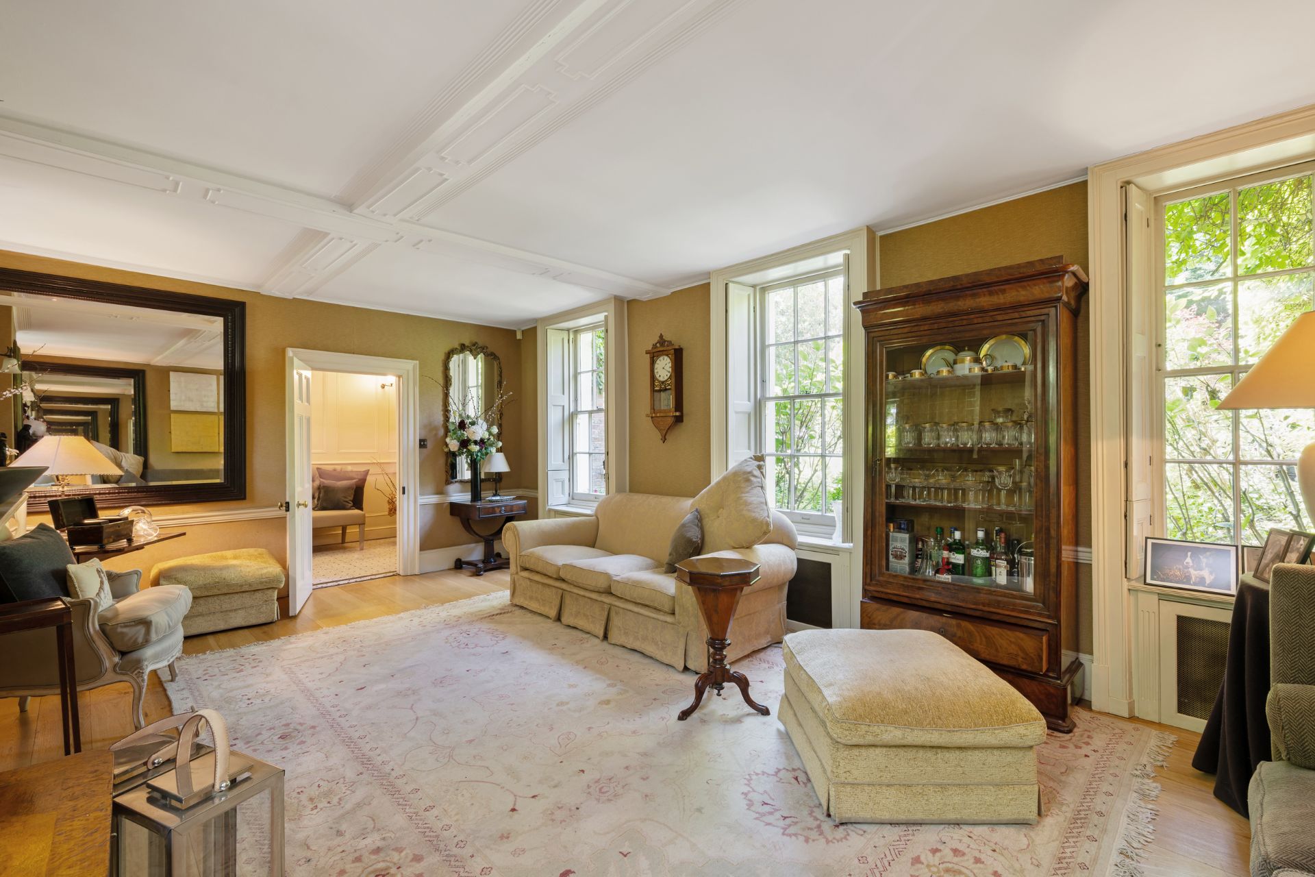 Living room with mustard yellow walls, a cream carpet, cream sofas, and an antique glass display cabinet