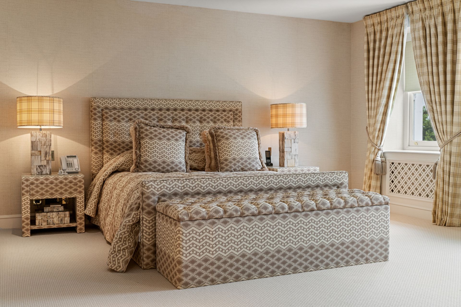 Bedroom with taupe patterned headboard, matching cushions, and a matching ottoman