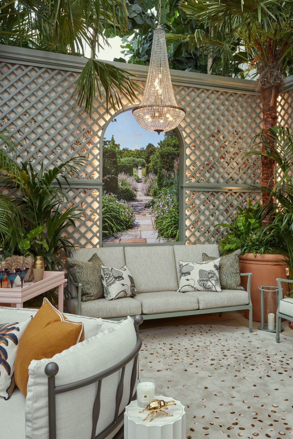 Garden space with crystal chandelier, wall trellis, cream sofas, potted ferns and a pale pink bar cart