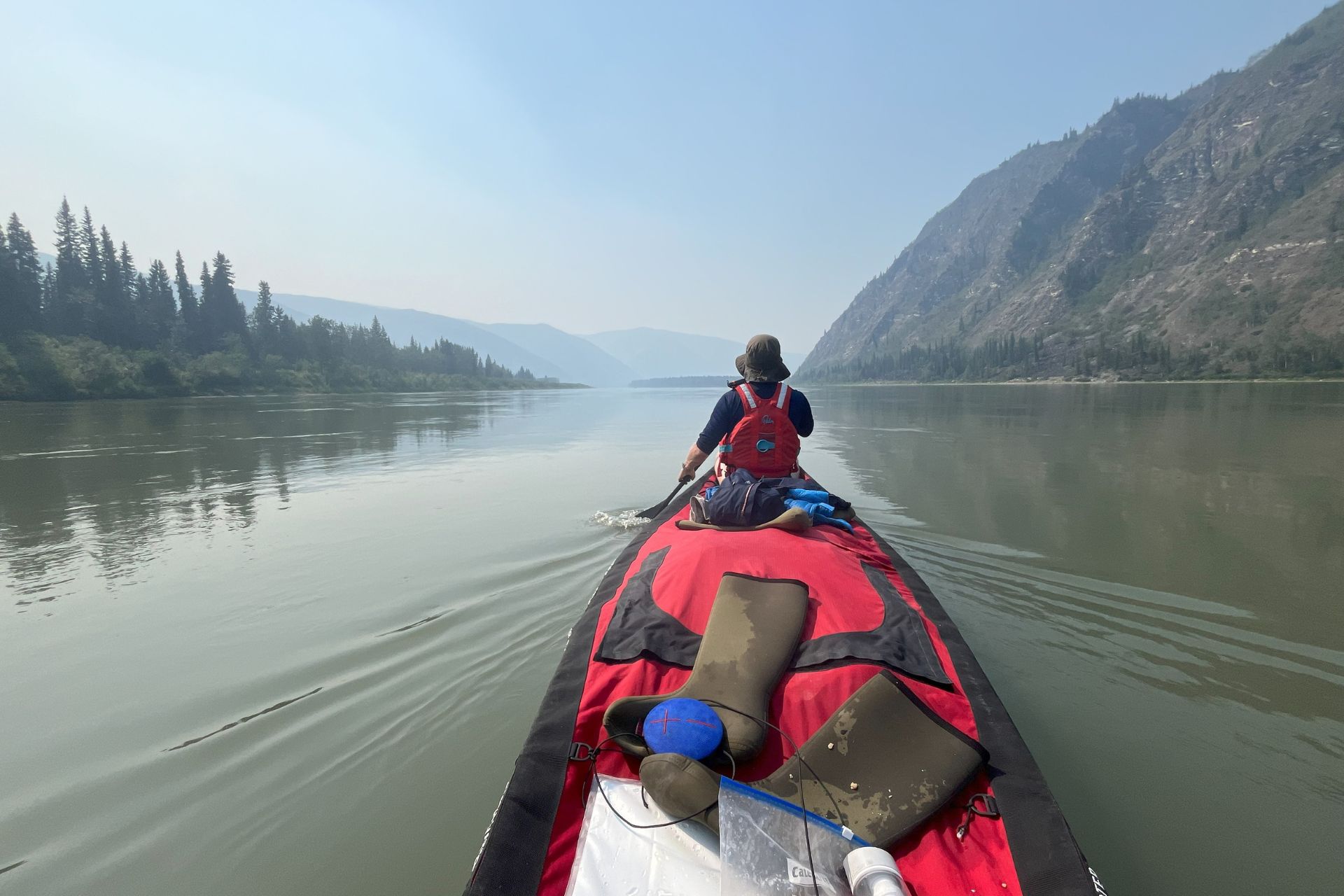 Canoest paddling down a river lined by mountains and trees