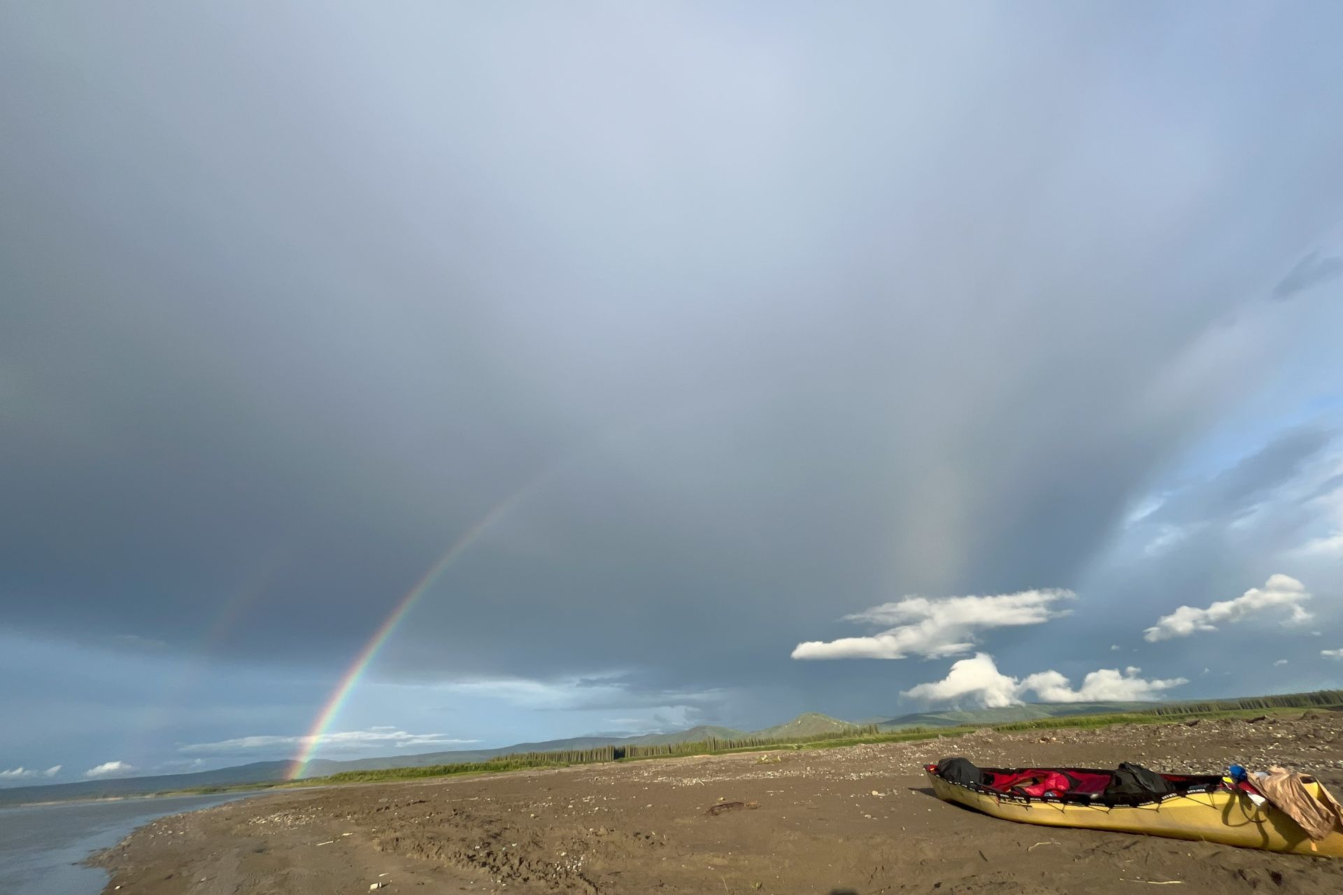 Canoe on a river bank with a rainbow in the distance