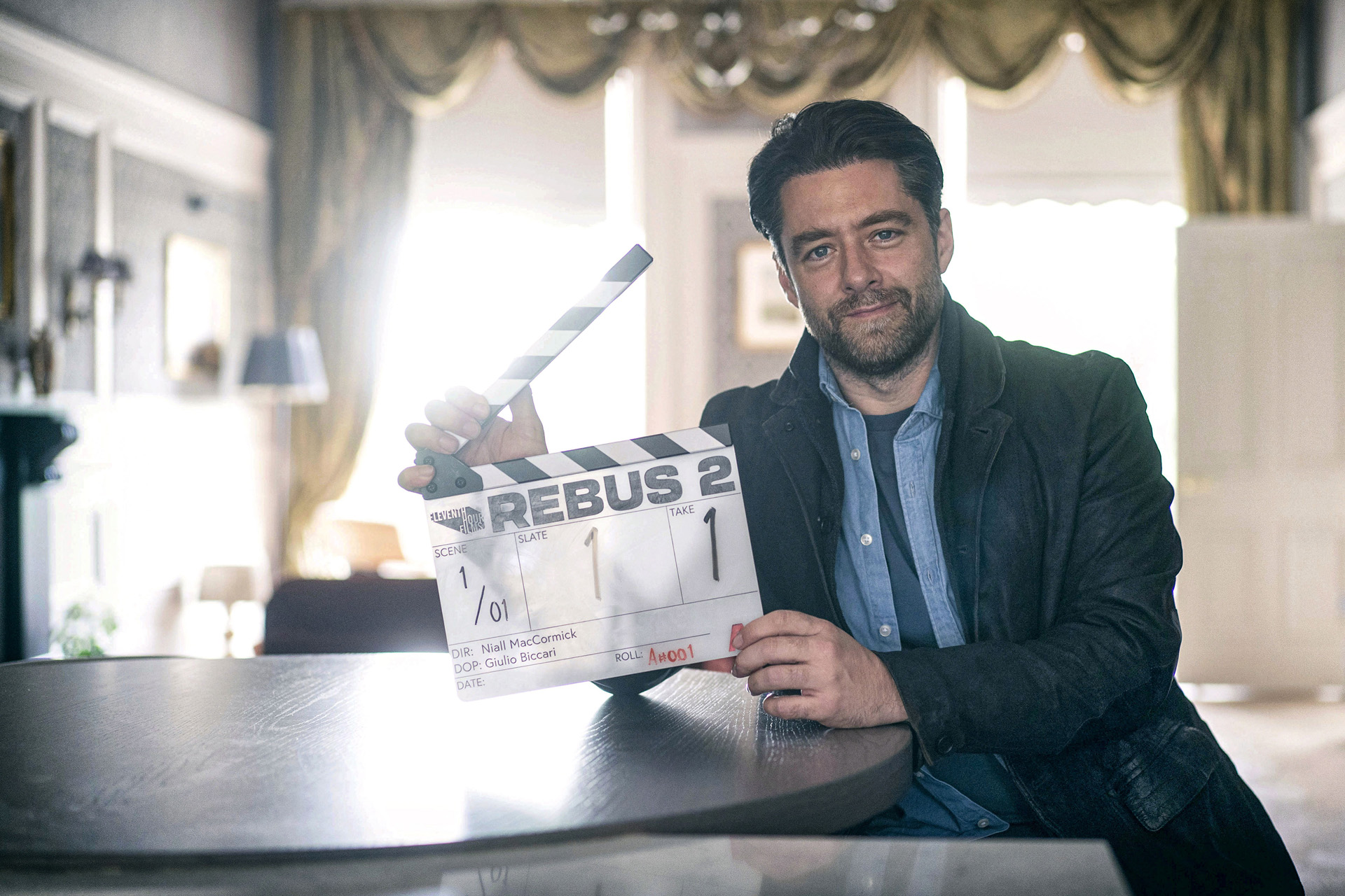 Richard Rankin holding a clapper board for Rebus Series 2