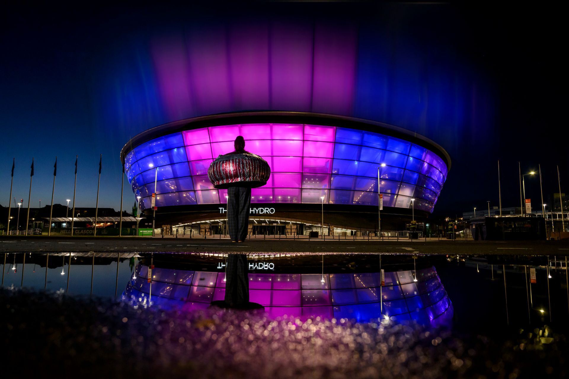 A night shot of the Hydro in Glasgow lit up with blue and pink