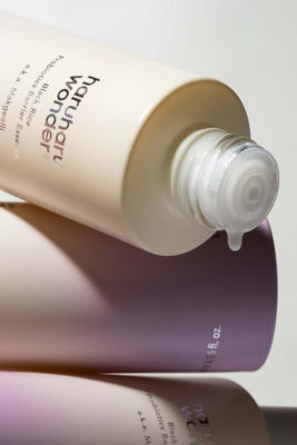 Skincare bottles stacked messily with one bottle open and dripping liquid