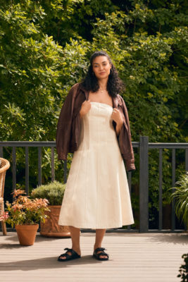 Woman standing on decking wearing dress, jacket and sandals | M&S x eBay