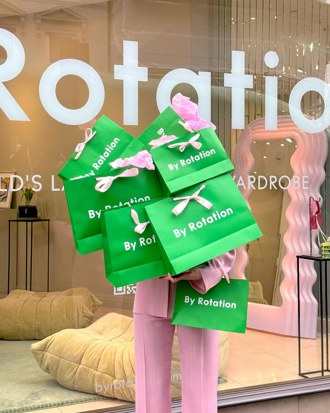Woman in pink suit holding mountain of green bags