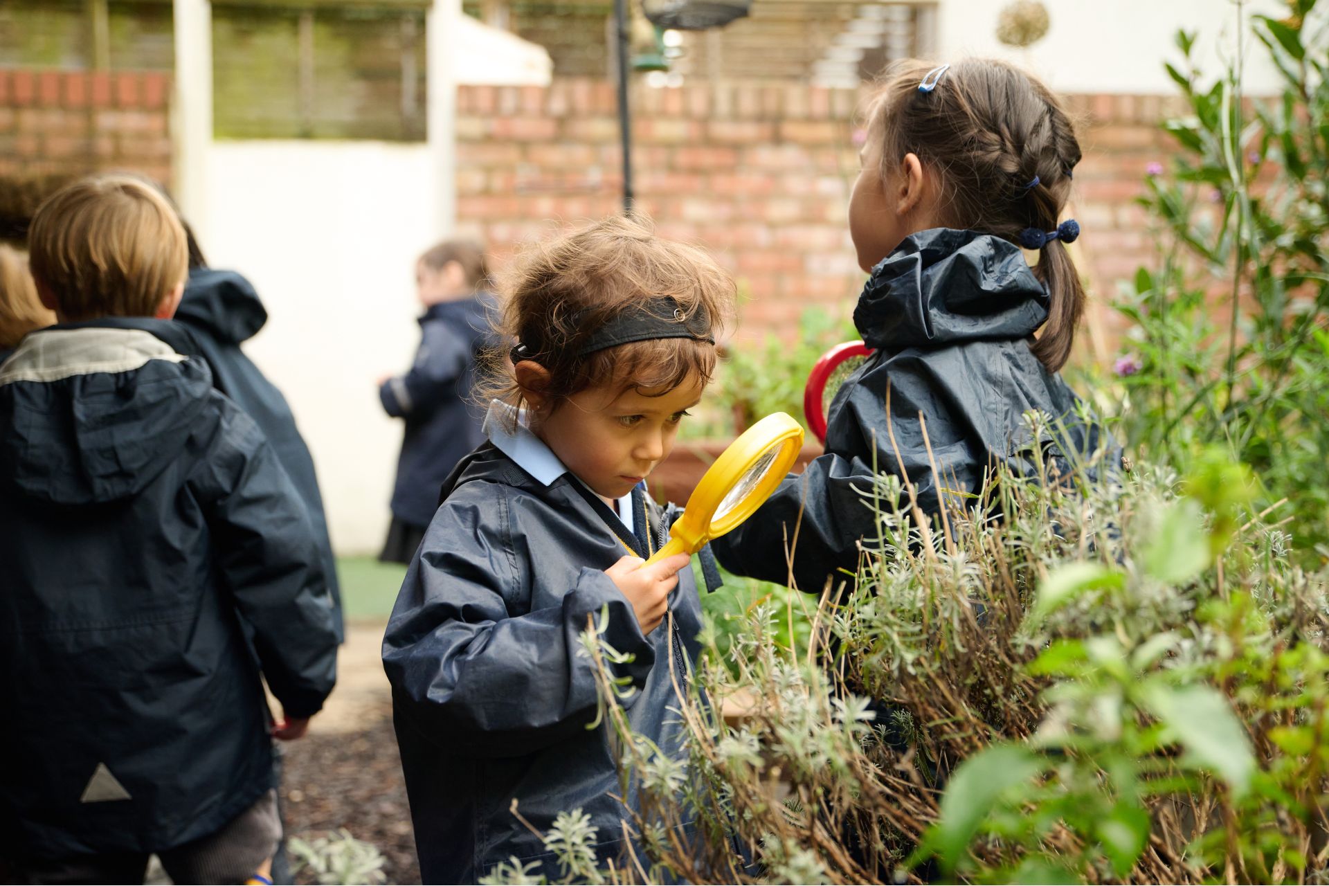 a young boy with brown hair looks through a yellow magnifying glass at some plants