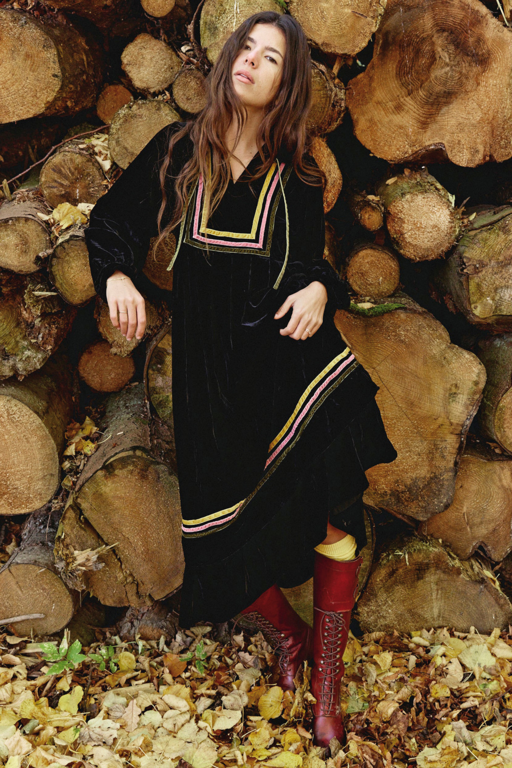 Woman wearing black dress stood in front of log pile