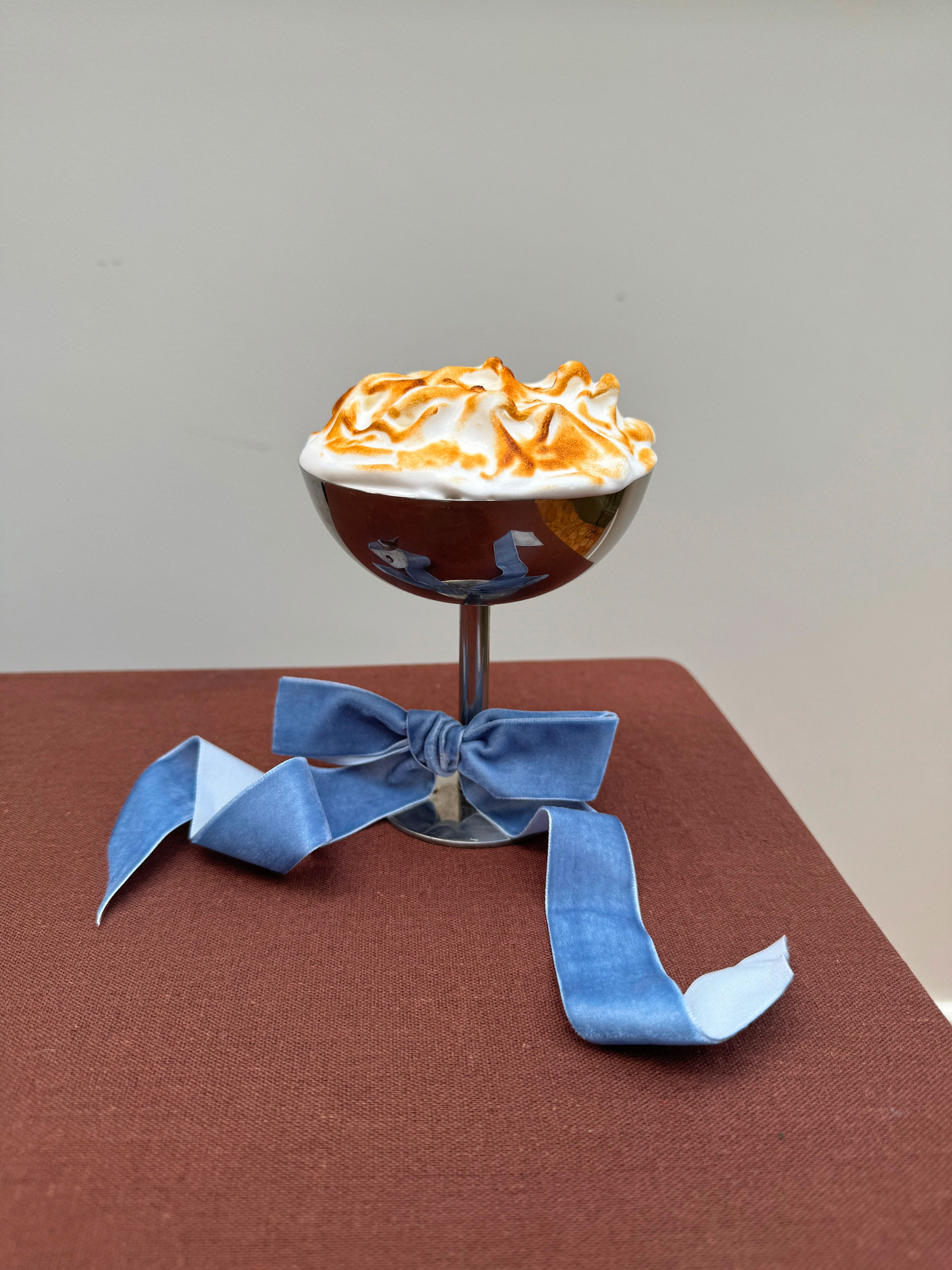 A meringue in a metal serving glass with a blue ribbon tied around it