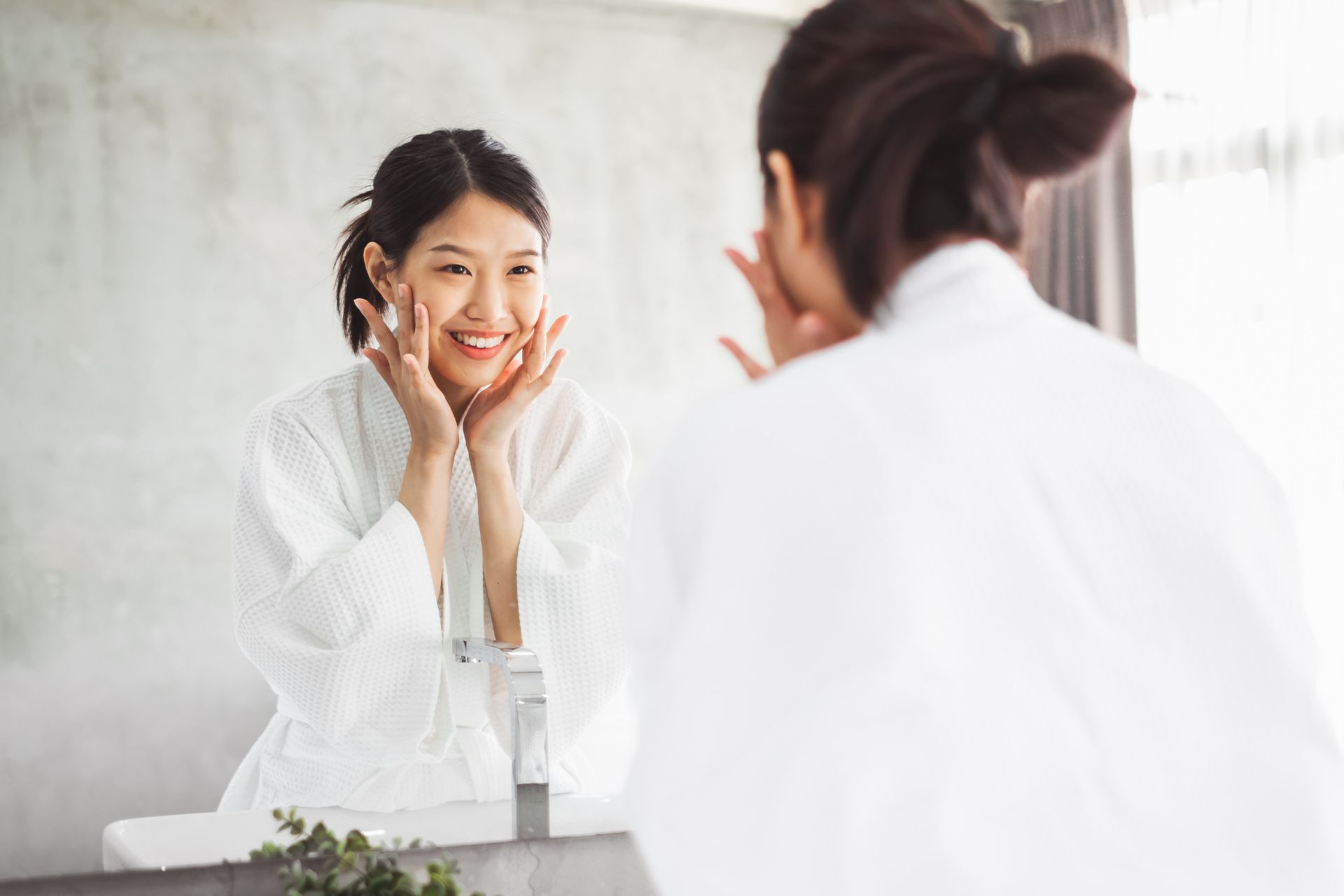 Woman in a white robe applying moisturiser in a mirror